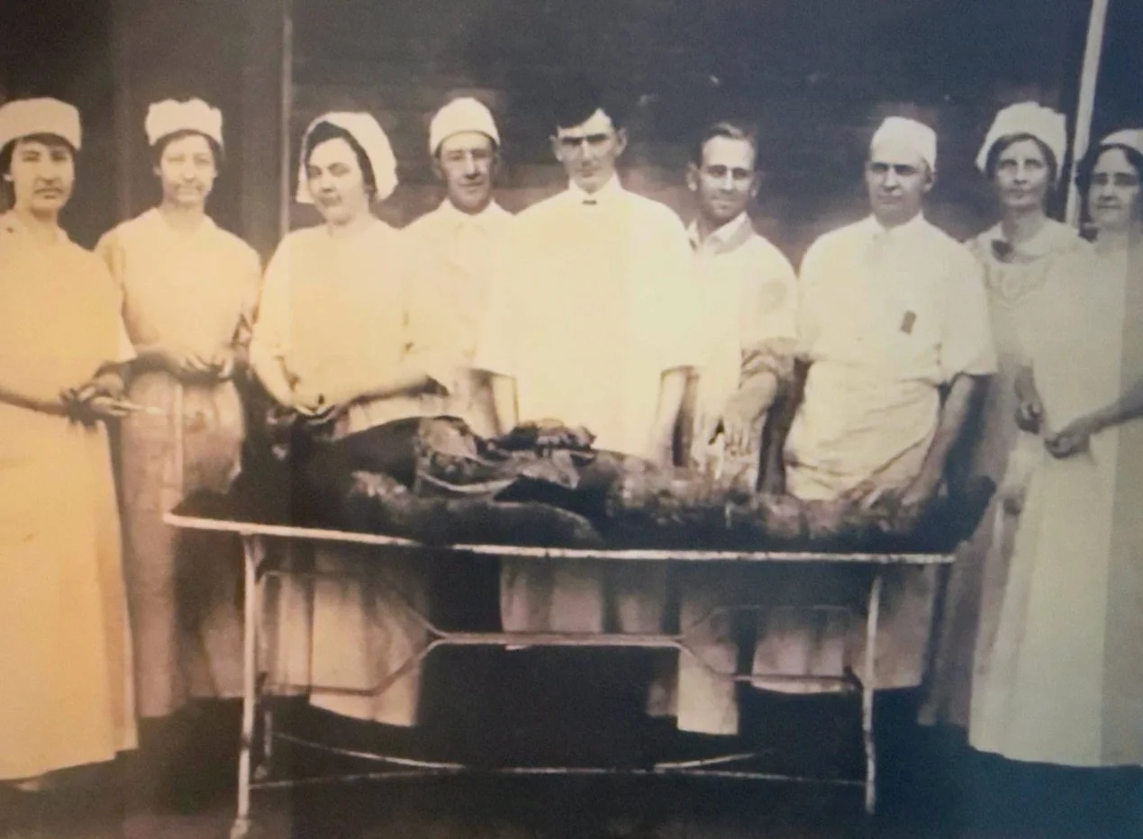 Group of medical staff in vintage uniforms standing around a patient lying on a table with surgical tools, in a historical operating room.