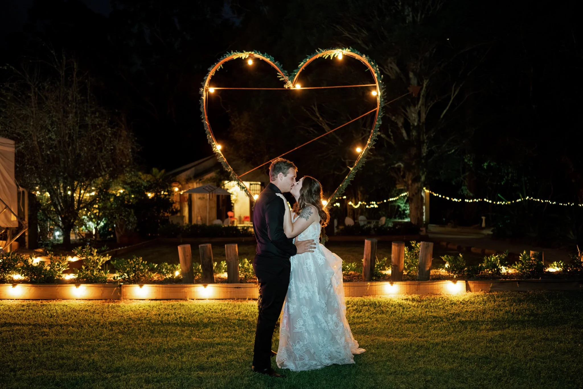 Bride and groom share a romantic kiss under heart-shaped lights at Kangy Gardens wedding in Hunter Valley.