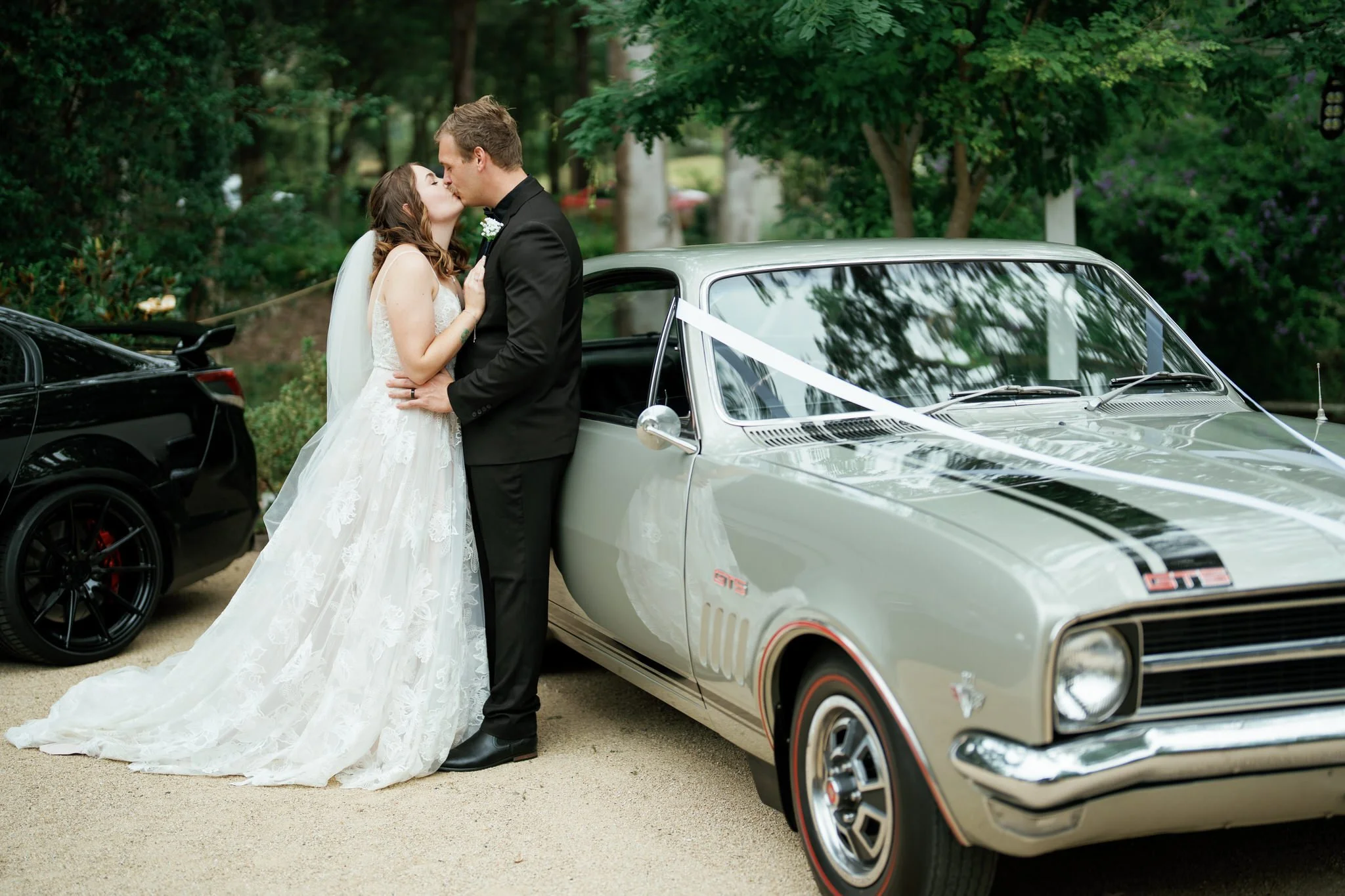 Bride and Groom Kiss Beside Classic Wedding Car at Kangy Gardens