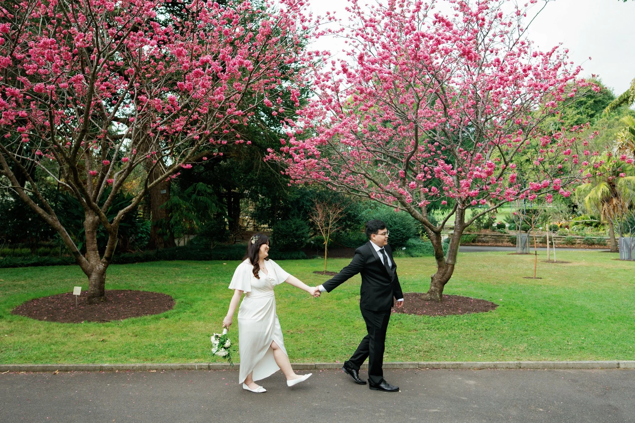 Candid Wedding Couple Walking Under Cherry Blossoms at Botanic Garden Sydney Palm House