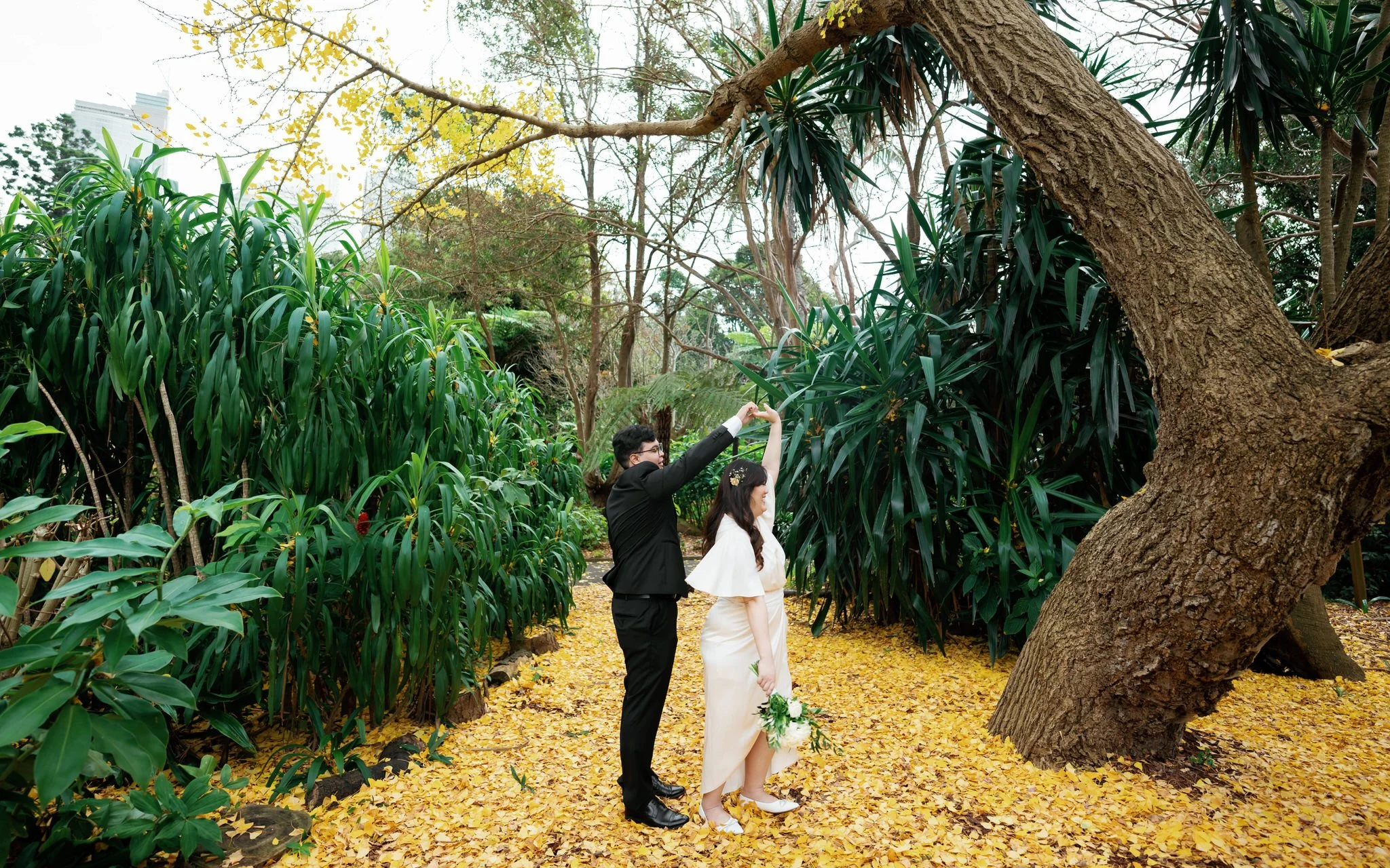 Candid wedding moment under yellow autumn leaves at Palm House, Sydney Botanic Garden