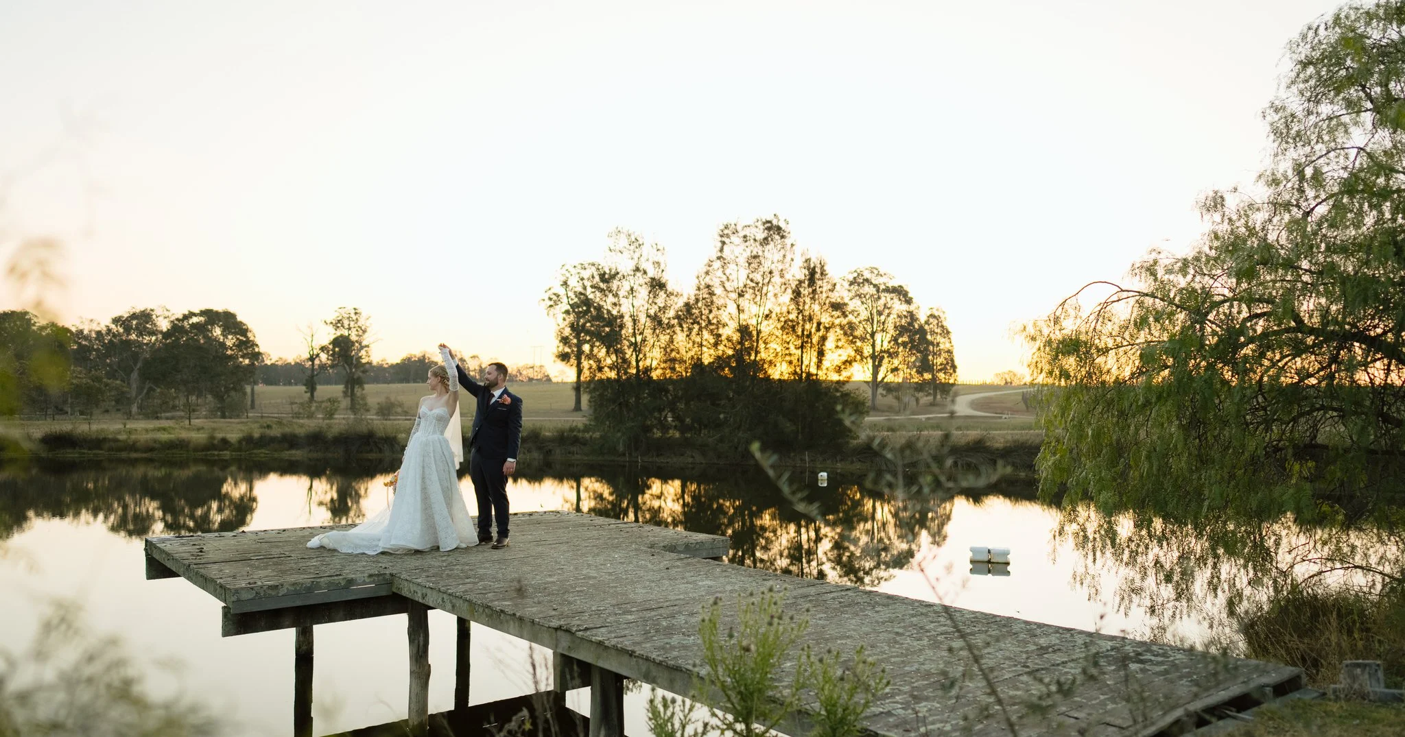 Groom twirling the bride on a wooden jetty at Squire's Vineyard, with sunset reflected in the water.