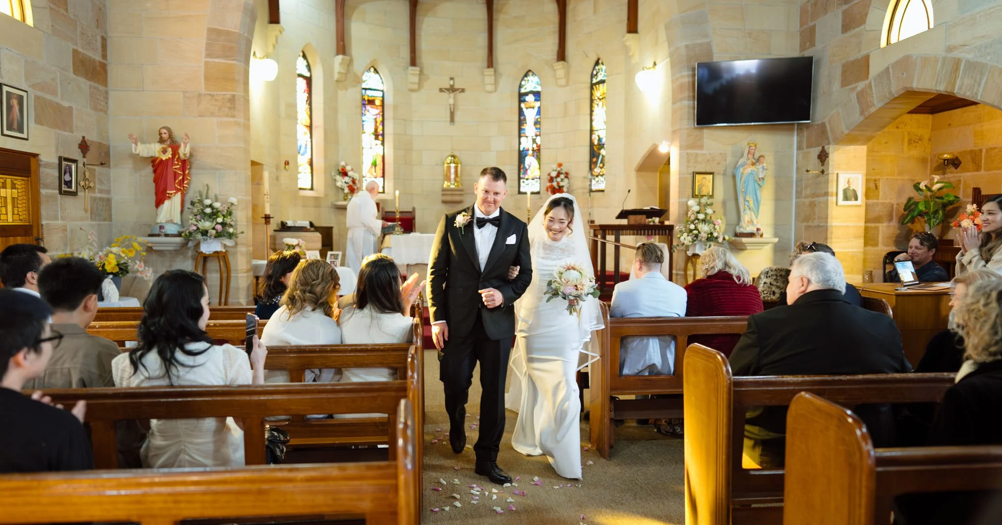 Newlyweds smiling as they walk down the aisle after their Merriwa Catholic Church wedding ceremony.