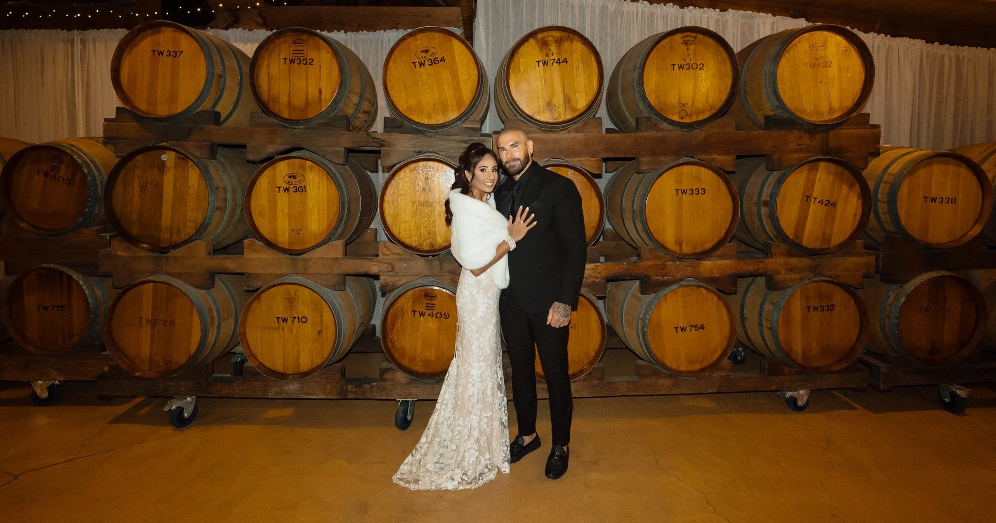 Bride and groom posing beside wine barrels inside Peppers Creek Barrel Room