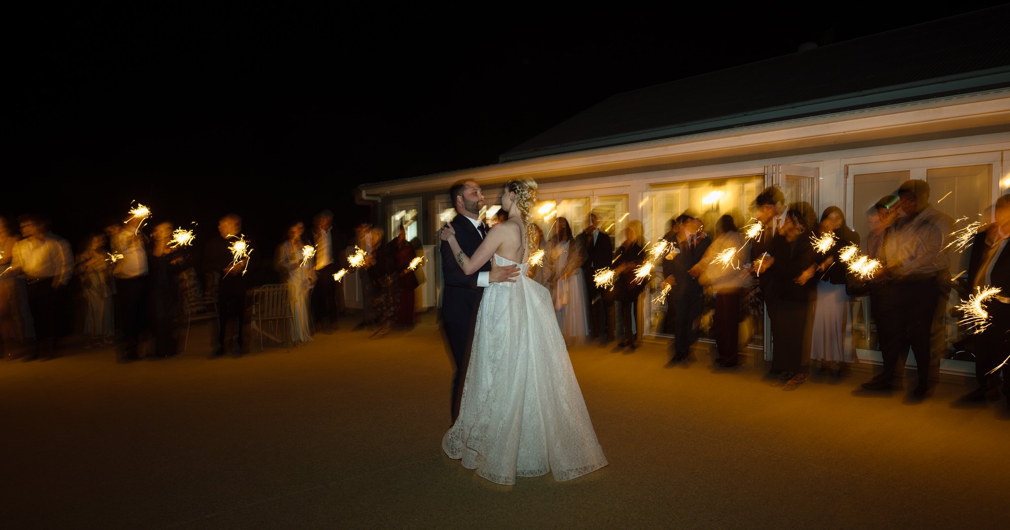 Bride and groom dancing outside Squire's Vineyard at night, surrounded by guests holding sparklers.