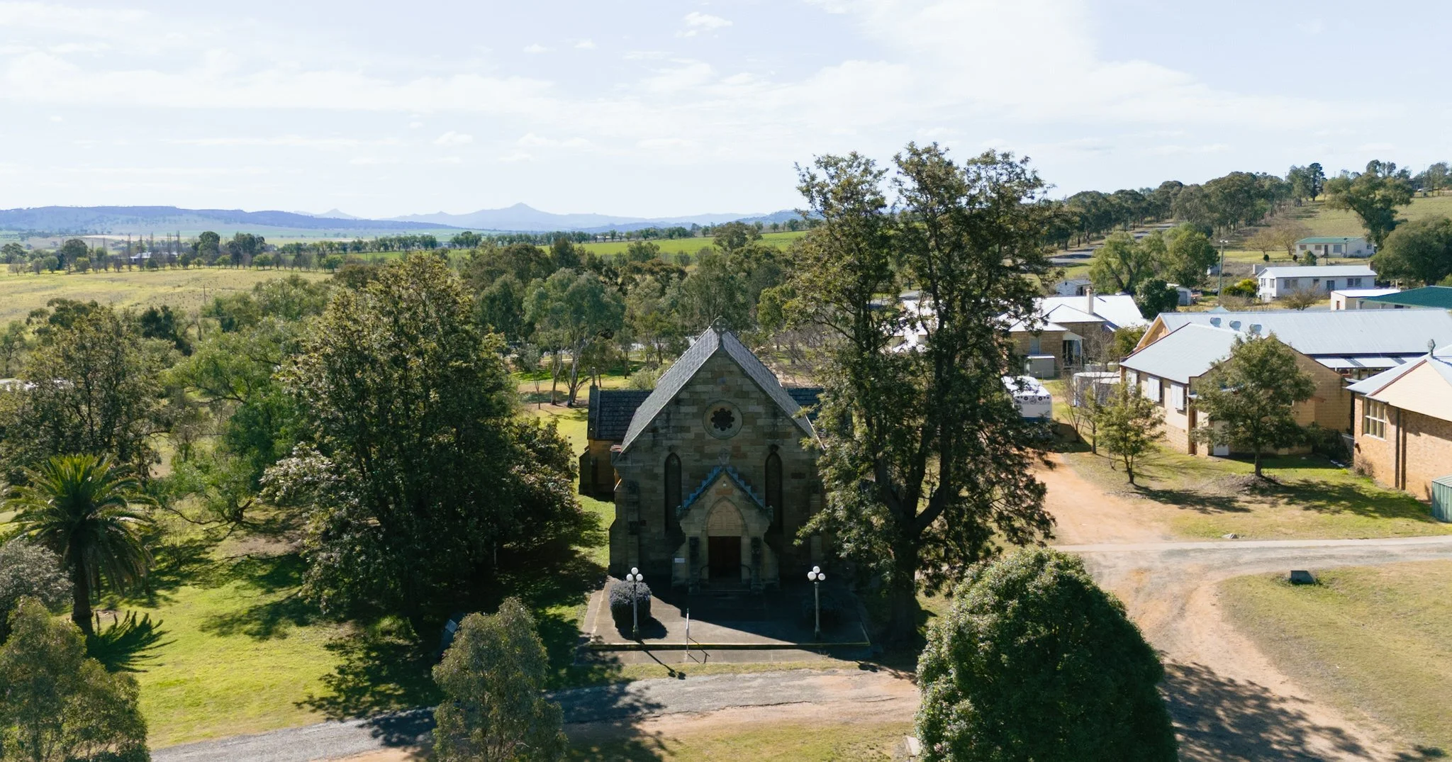 Aerial view of Merriwa Catholic Church surrounded by trees and the country landscape of Merriwa NSW.