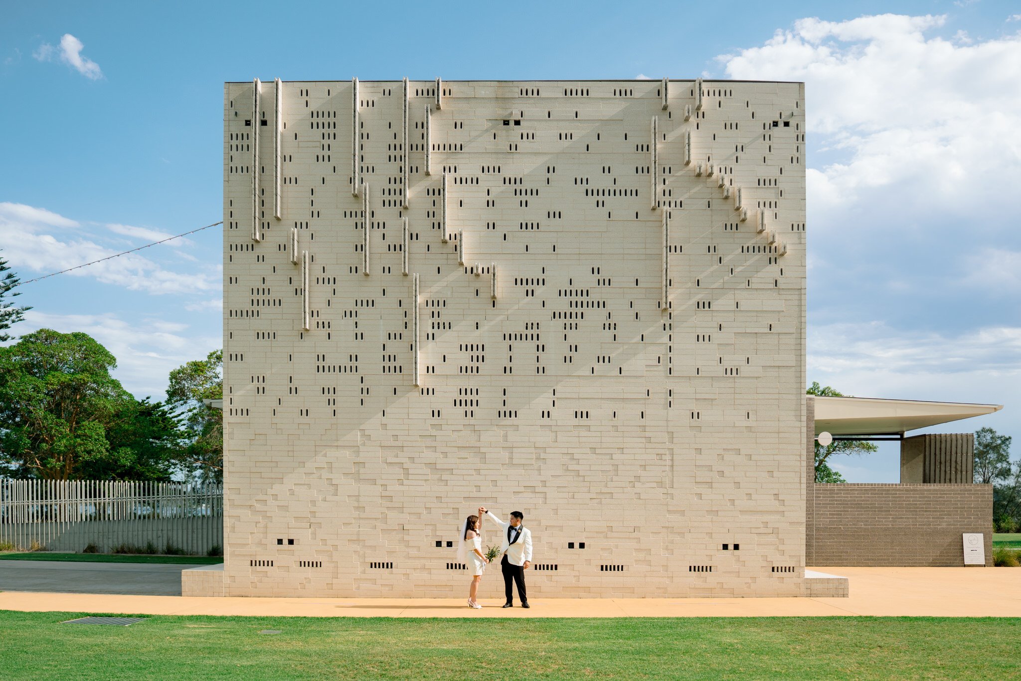 A couple shares a quiet, joyful moment in front of a striking modern architectural wall at Speers Point Park. Clean lines, soft light, and open space create a timeless and elegant outdoor portrait setting.