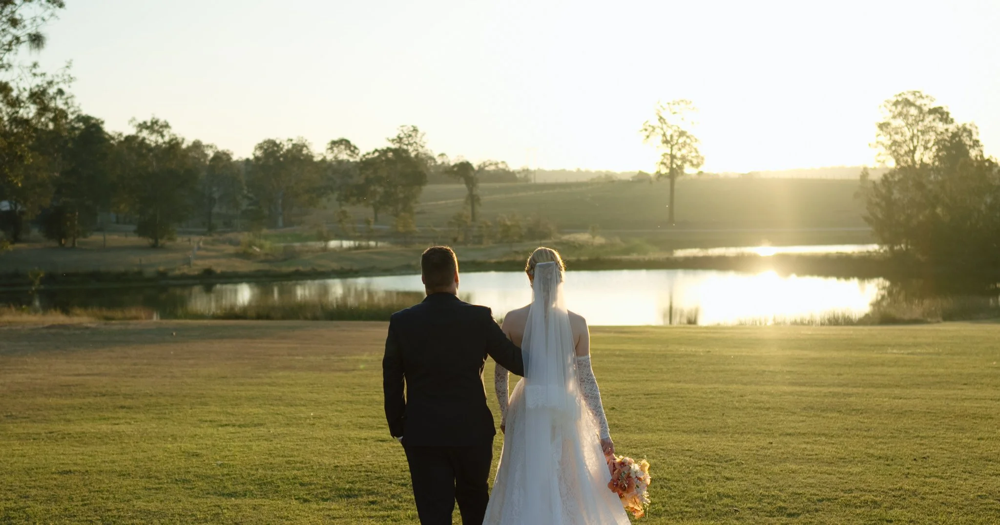 Bride and groom viewed from behind, standing together on the lawn overlooking the water at Squire's Vineyard.