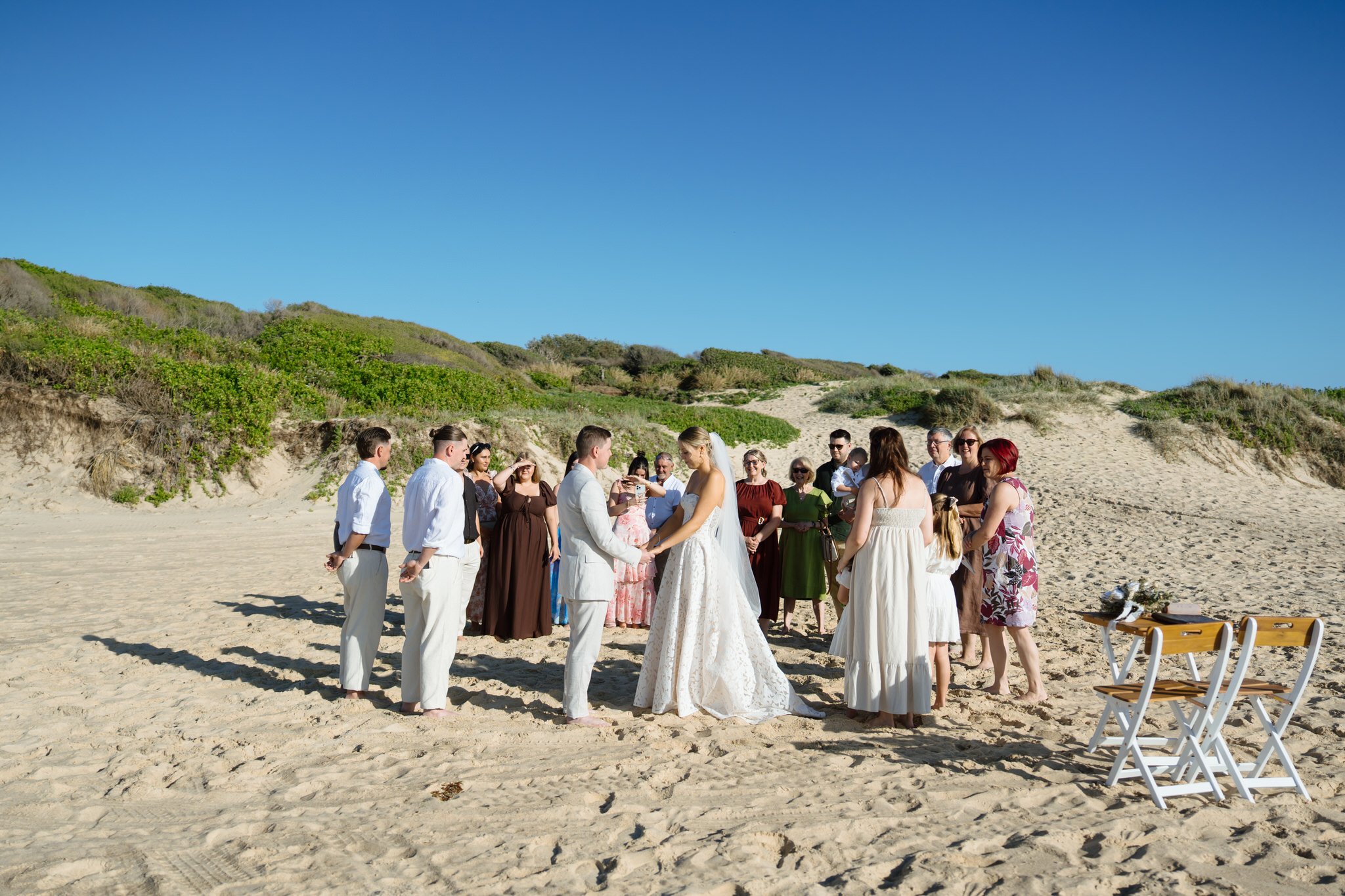 Couple exchanging vows surrounded by guests in a circle on the sand at Caves Beach