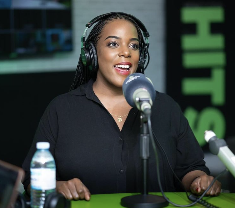 Woman with braided hair and headphones speaking into a microphone during a radio broadcast or podcast recording.