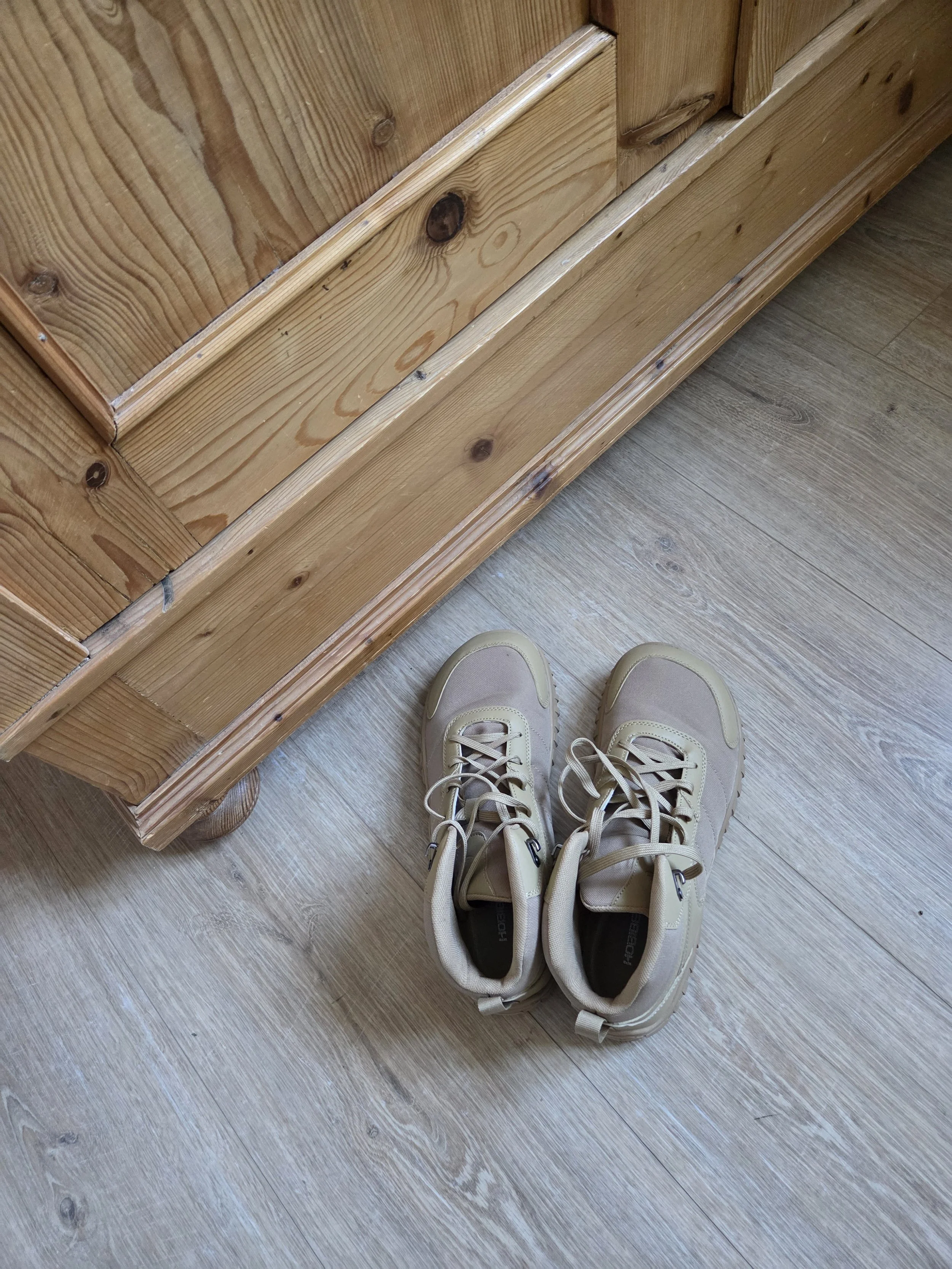 Ein Paar Schnürschuhe steht bereit auf einem Holzboden neben einem Holzmöbel.