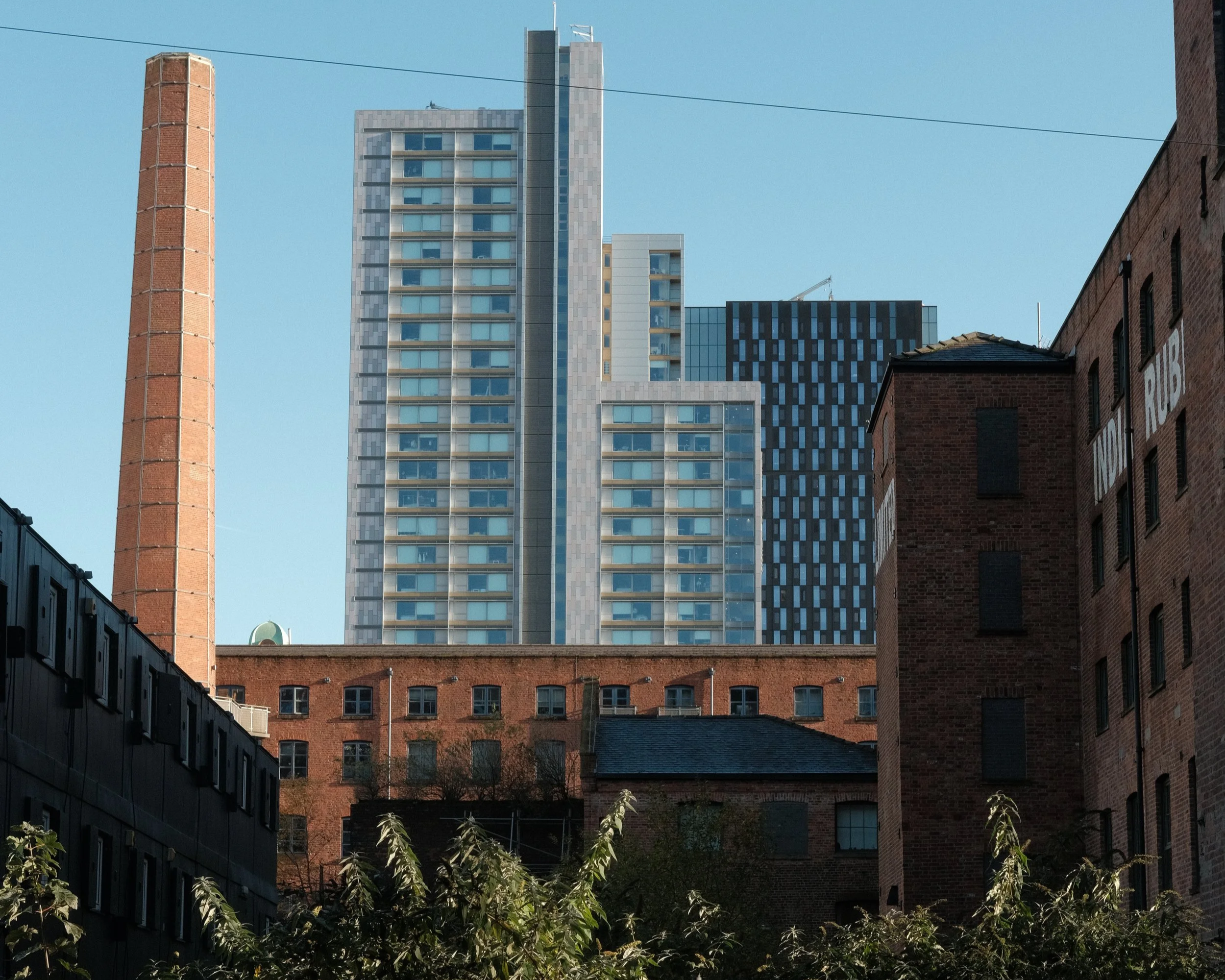A cityscape showing a mix of old brick buildings and modern high-rise glass skyscrapers, with a clear blue sky in the background.