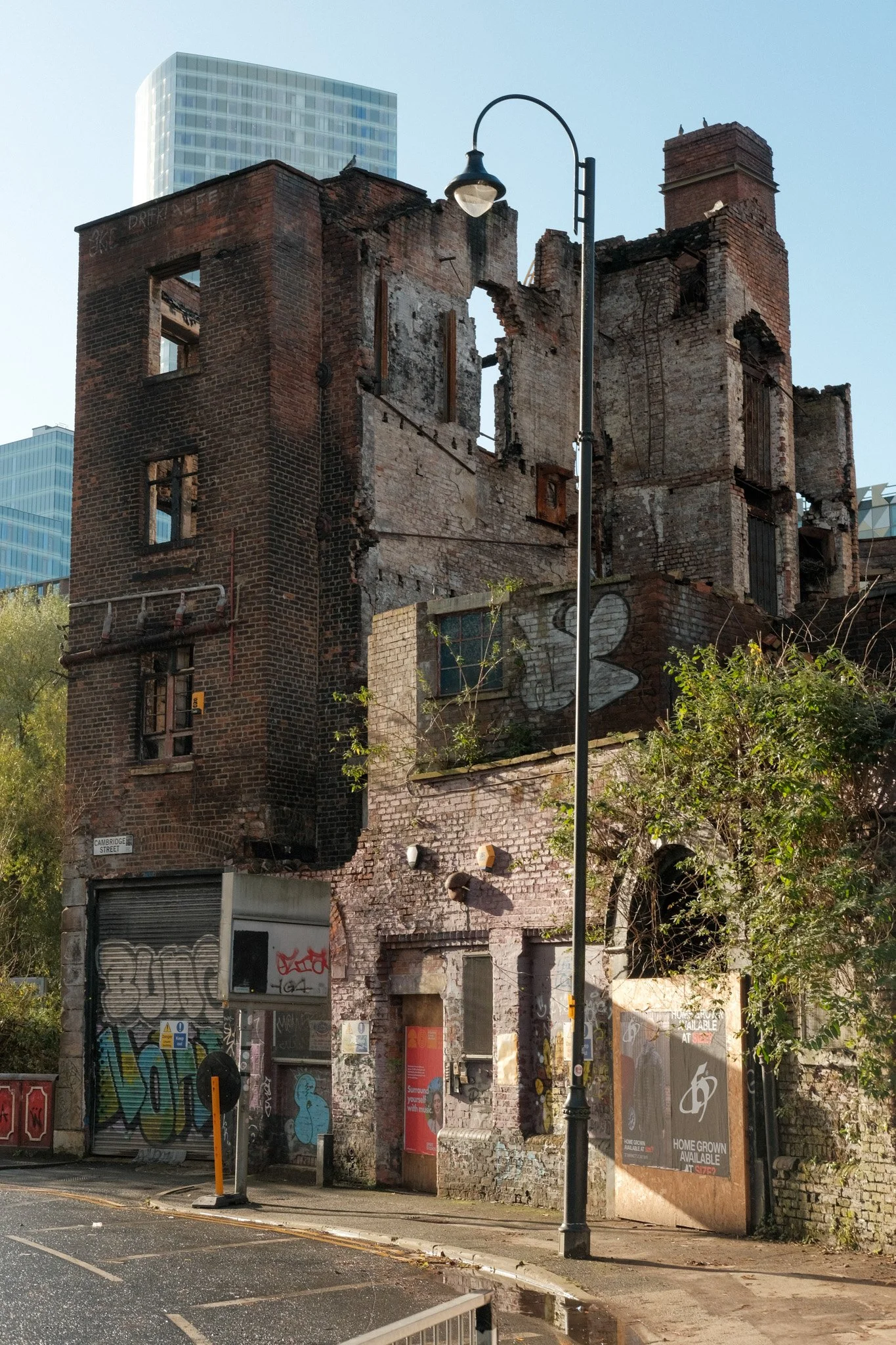 A partially destroyed old brick building with missing walls and windows, graffiti on the lower part, a streetlamp in front, and modern skyscrapers in the background.
