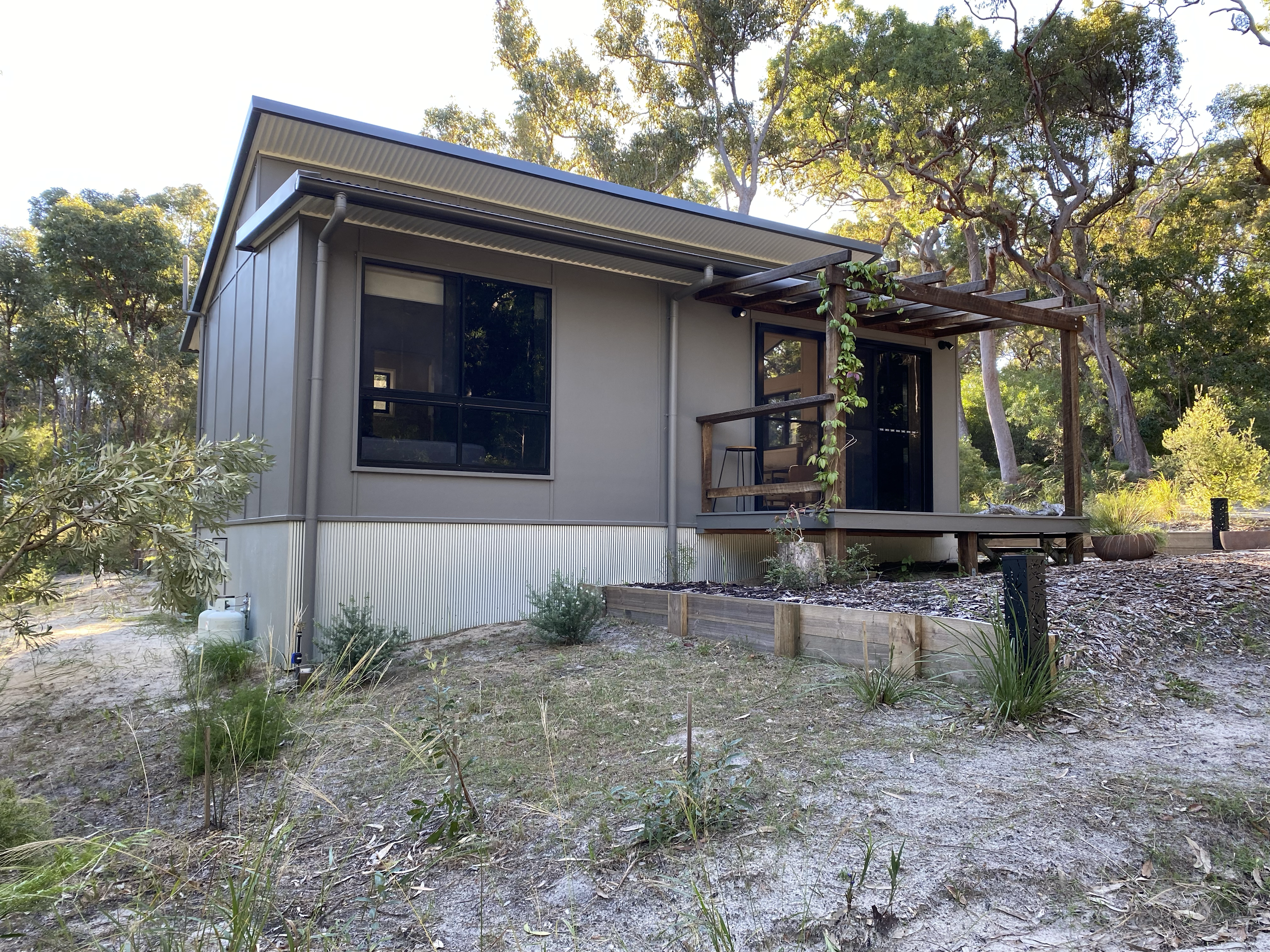 A modern house with metal siding, large windows, and a small porch with a roof, surrounded by trees and natural landscaping. Orchid Beach accommodation K'gari Fraser Island