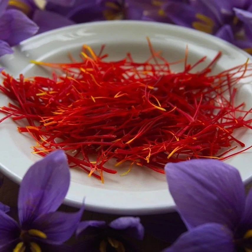 A white plate with a pile of red saffron threads, surrounded by purple flowers.
