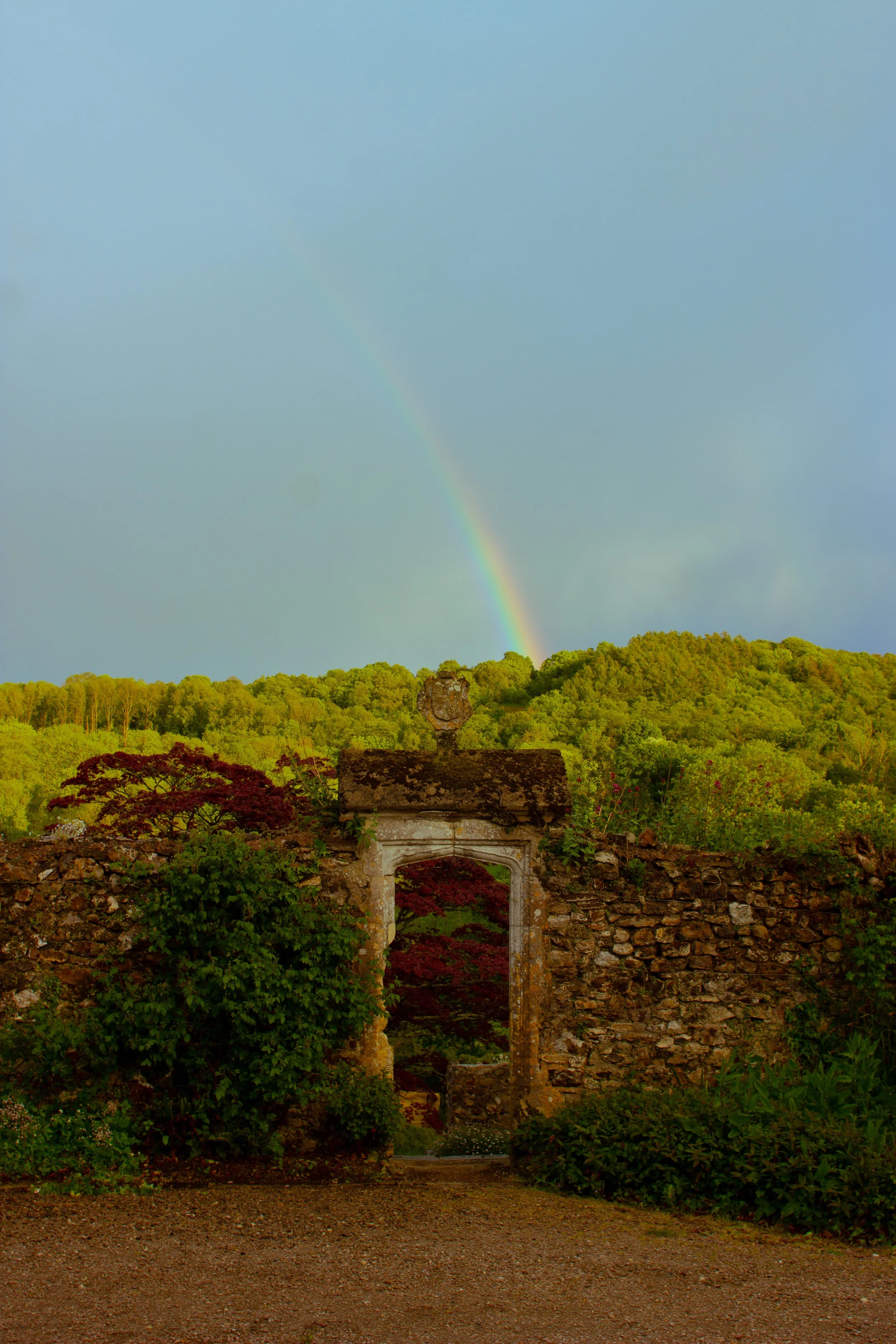 A sunset or sunrise rainbow over a lush green hill, with an old stone structure in the foreground.