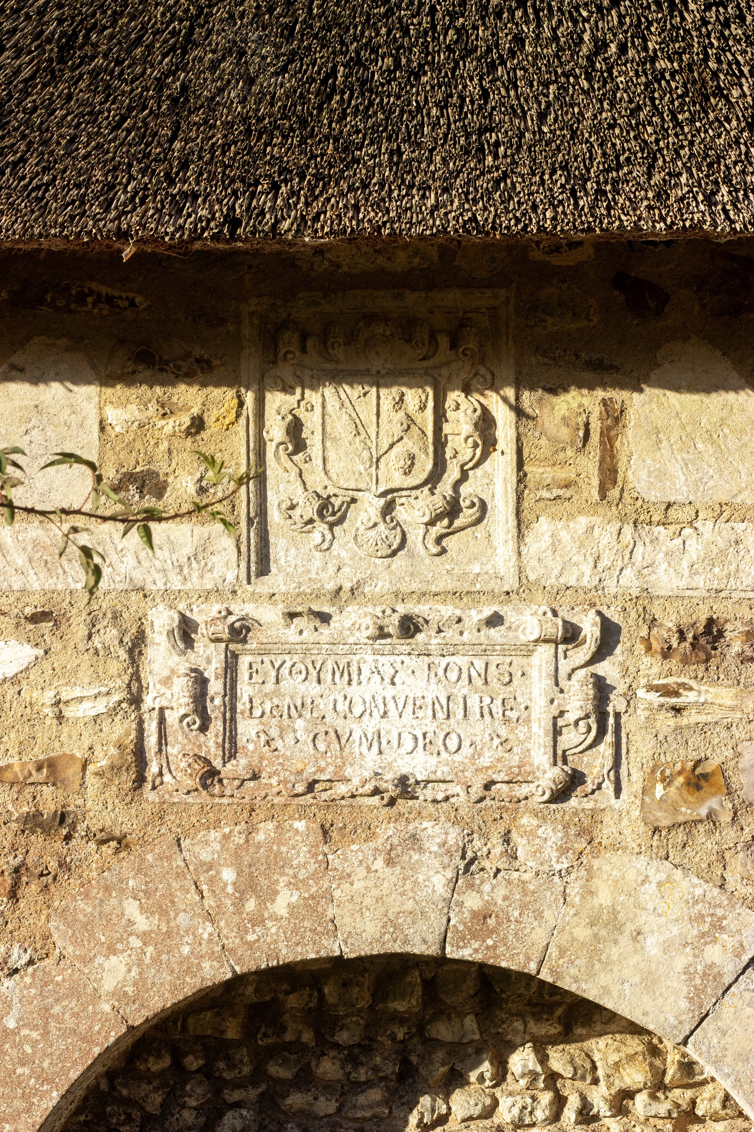Stone wall with a carved plaque containing a coat of arms and French inscription, part of an old historical building or monument.