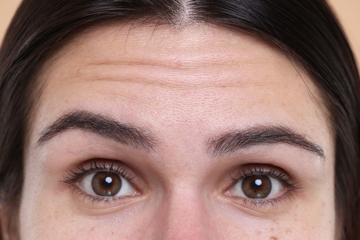 Close-up of a woman's eyebrows and eyes, showing the skin on her forehead and brown irises.