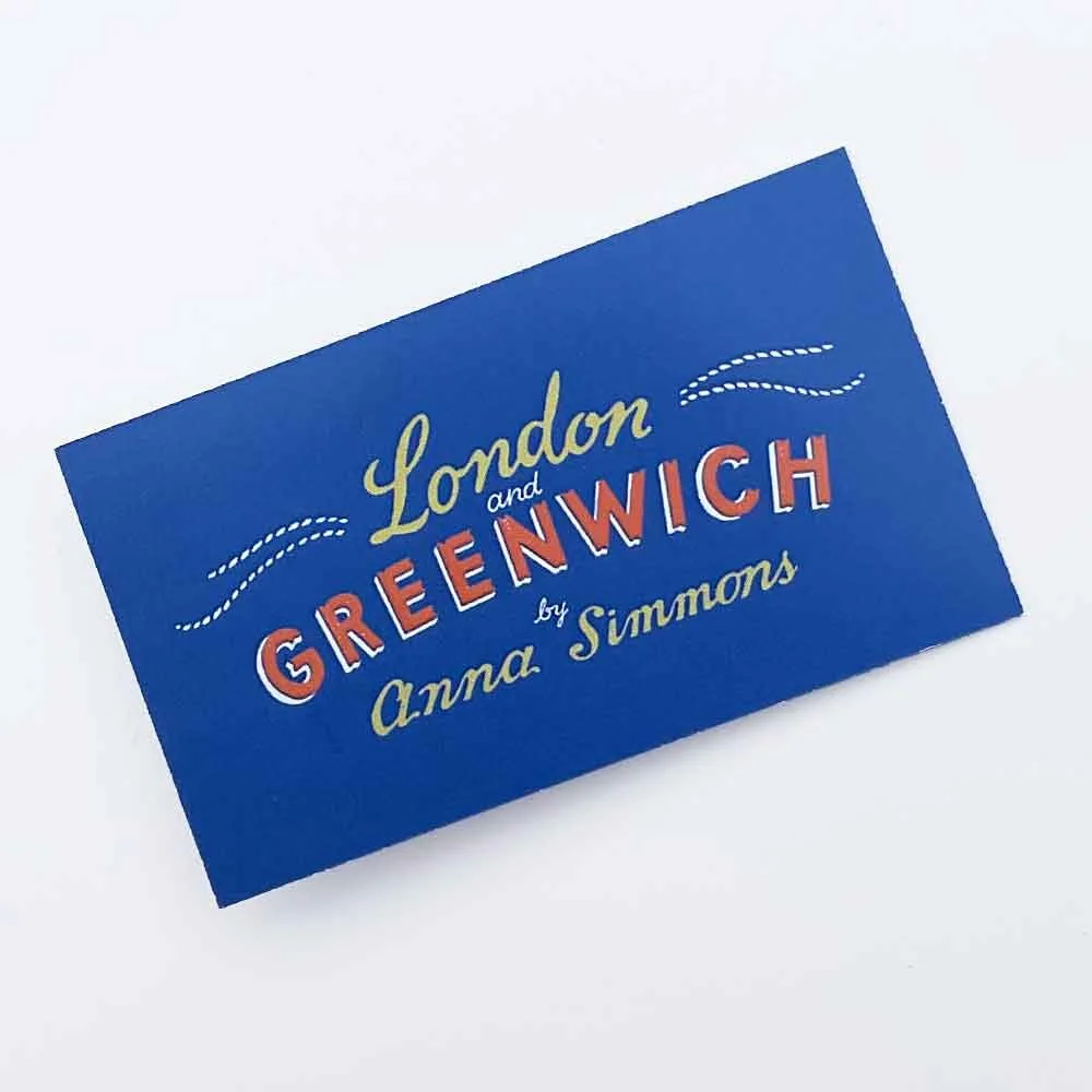 Photograph of a blue swing tag with orange, yellow, and white hand-lettered “London and Greenwich by Anna Simmons”, illustrated by Anna Simmons