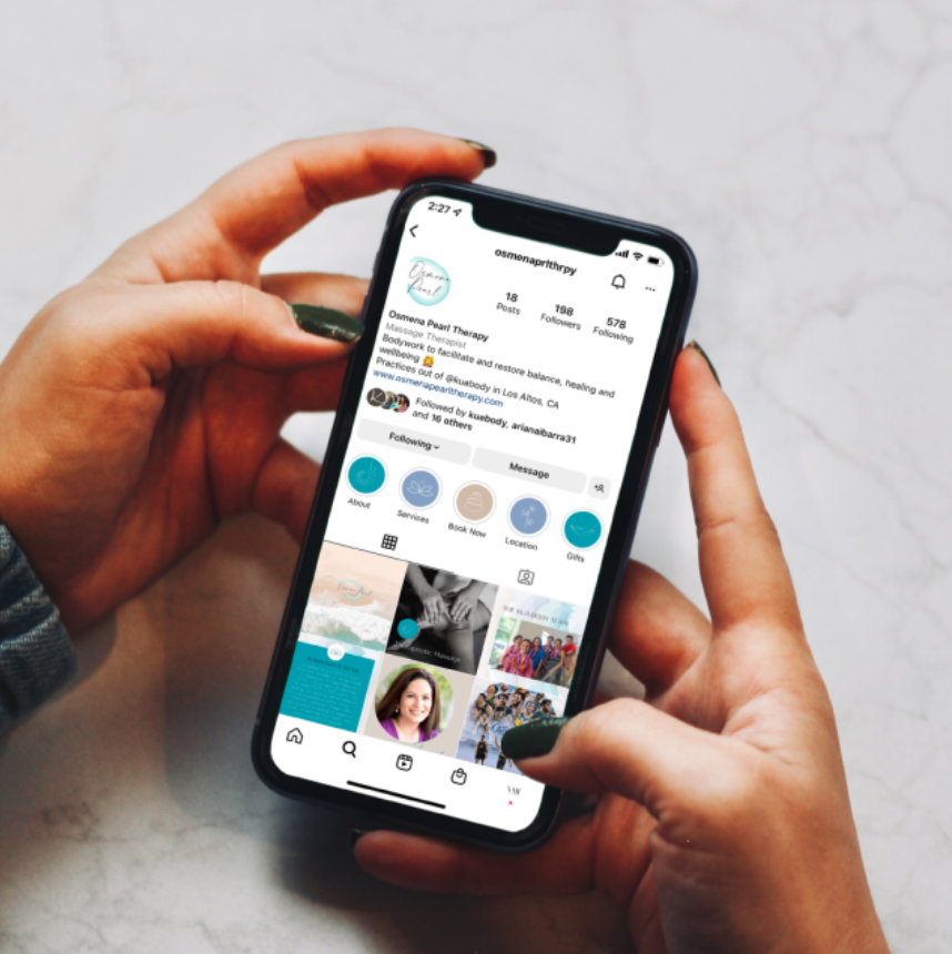 Hand holding a smartphone displaying an Instagram profile with several posts and engagement buttons on the screen.