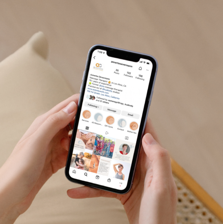 Person holding a smartphone displaying an Instagram profile page, showing profile details, navigation buttons, and posts.