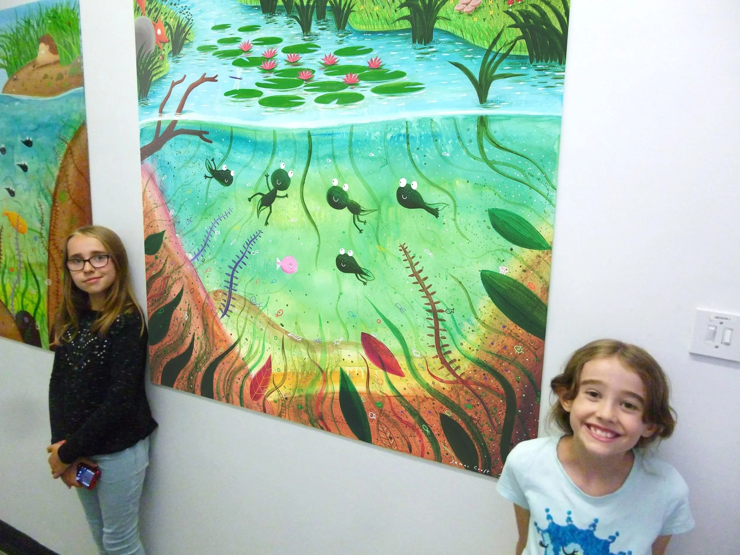 two girls looking at paediatric hospital corridor murals with frog and pond scene by James Croft