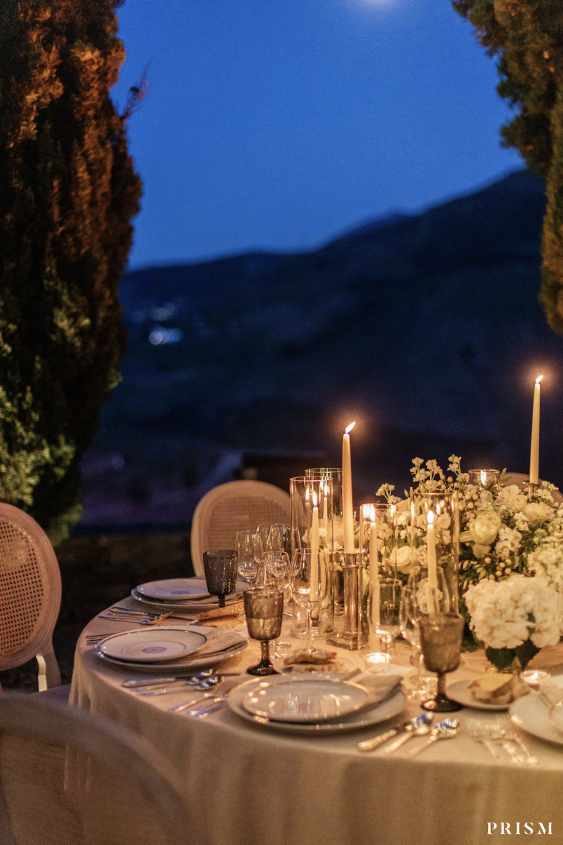 An outdoor wedding dining table decorated with white flowers, tall candles, and elegant glassware. Luxury Wedding Planner for Mediterranean & Destination Weddings