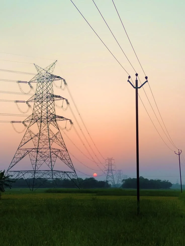 Photographie de lignes à haute tension dans un champ au coucher du soleil, avec un ciel pastel.