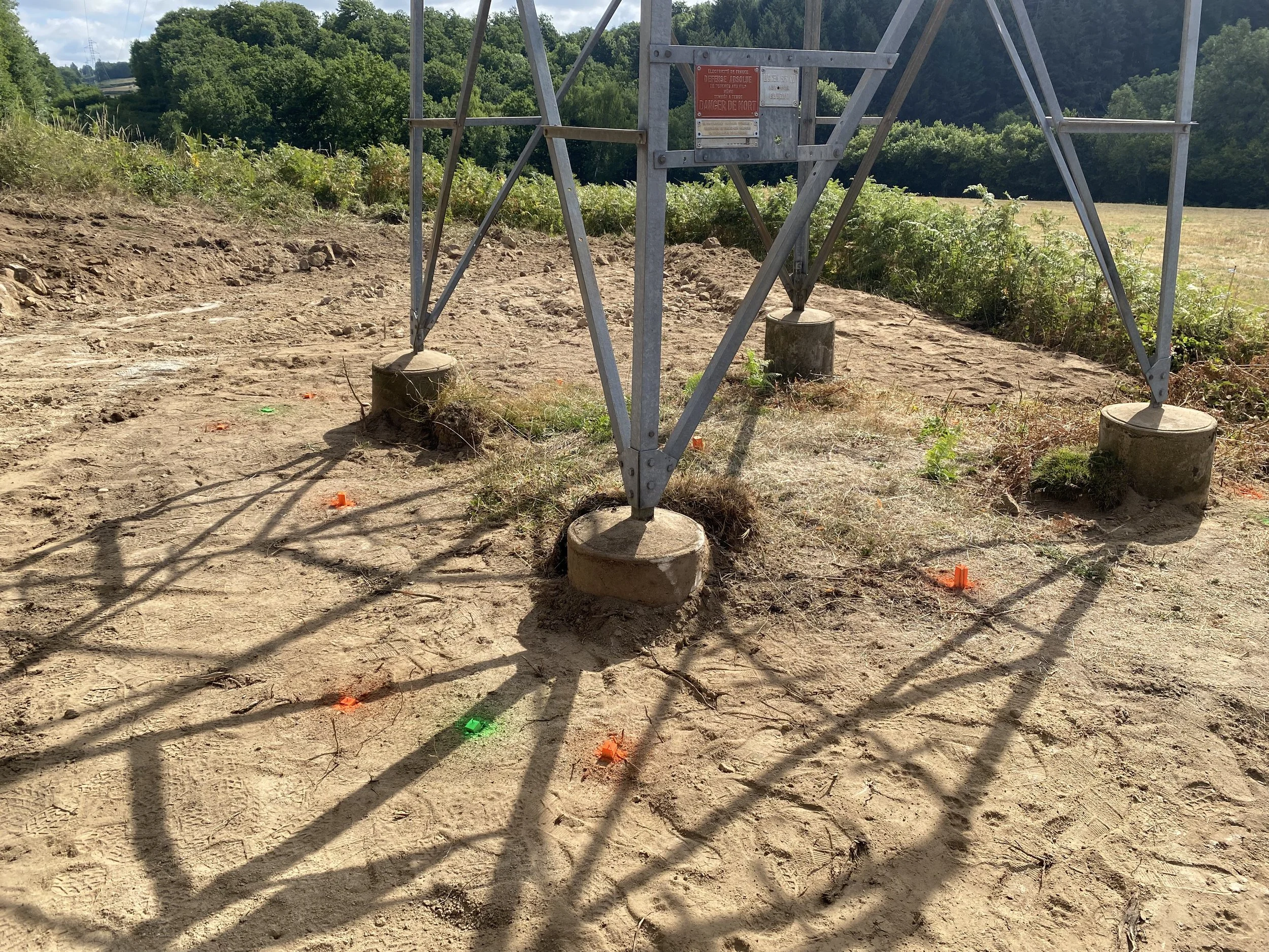 Une structure métallique sur un terrain en terre, avec des signaux colorés au sol et un paysage verdoyant en arrière-plan.