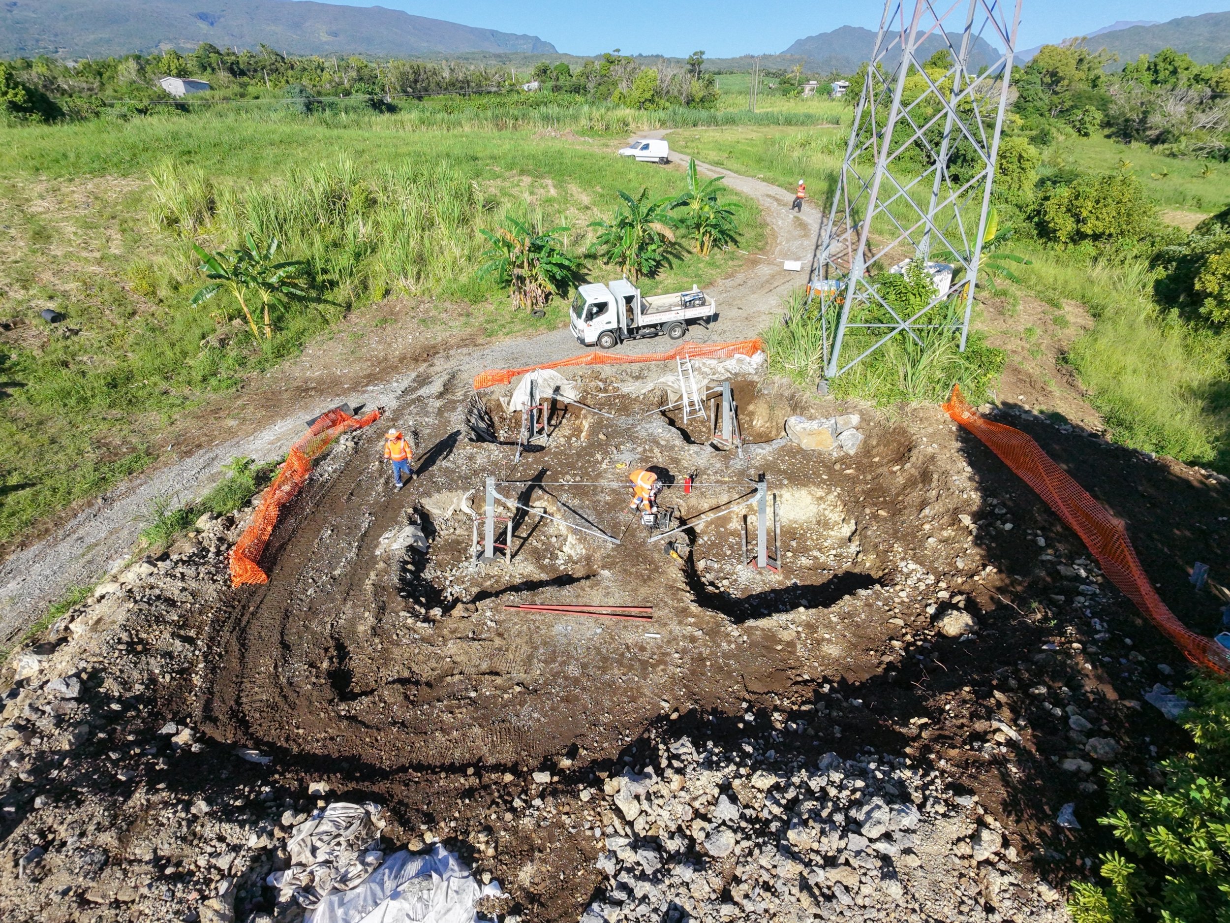 Travaux de construction ou de réparation sur une station électrique en plein air, avec des ouvriers en safety vest et casque, entourés de matériel et de barrières orange. Lebon Services - votre prestataire pour vos chantiers de lignes électriques