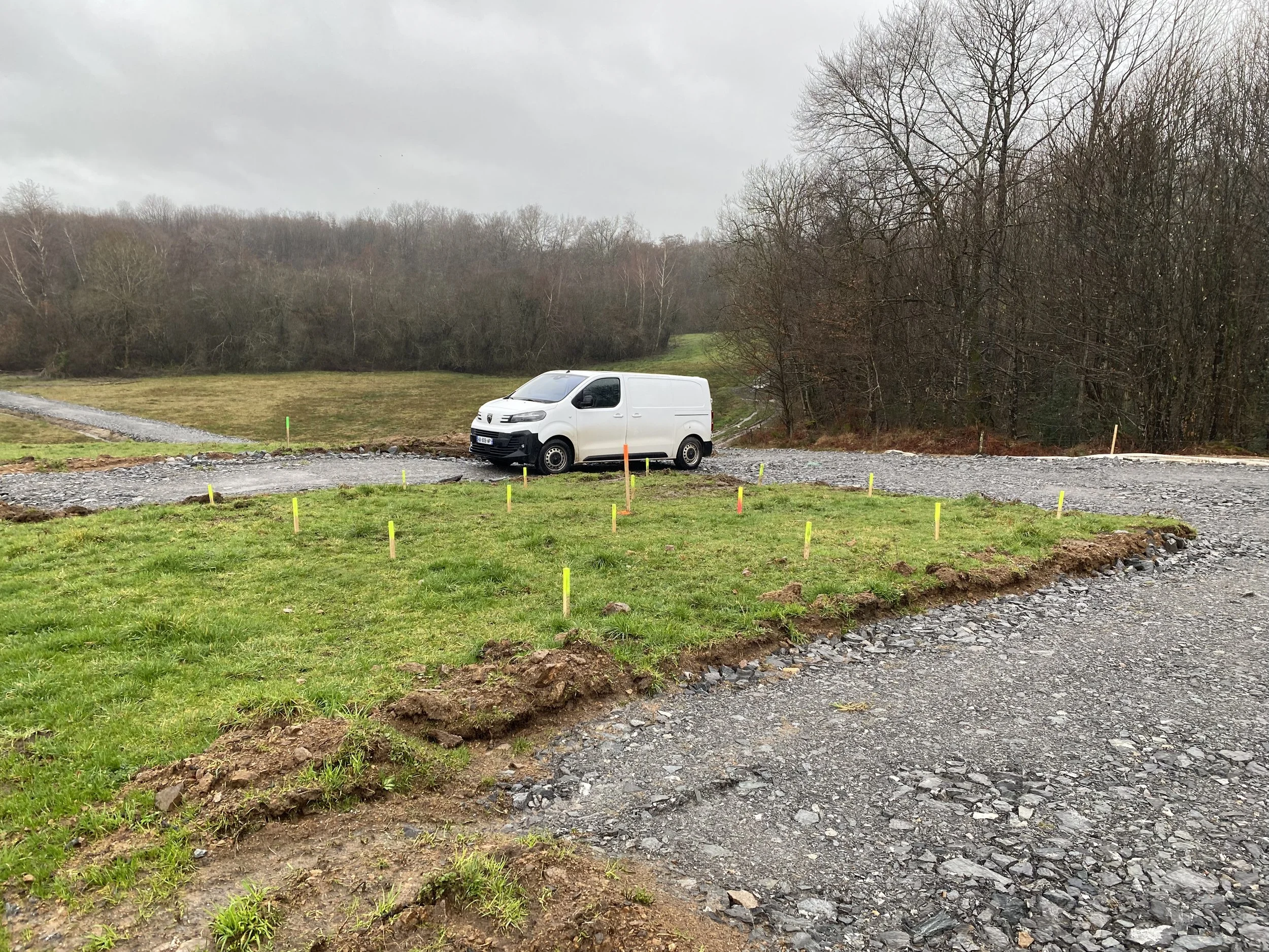 Une voiture blanche stationnée sur un terrain en construction avec des piquets colorés, entourée d'arbres nus sous un ciel gris.
Lebon Services - votre prestataire pour vos chantiers de lignes électriques haute tension.