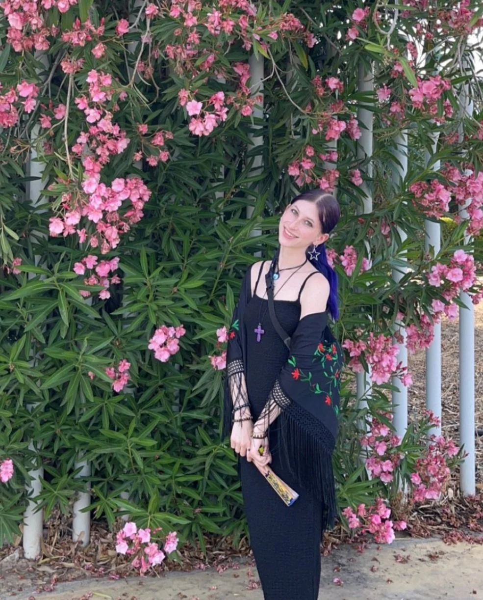 a woman smiling in front of a wall of pink flowers