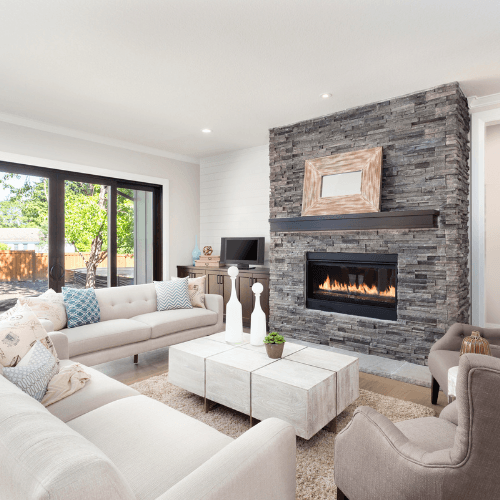 The image shows a modern living room with light-colored, neutral-toned furniture. There are two light beige sofas and an armchair arranged around a square white coffee table.