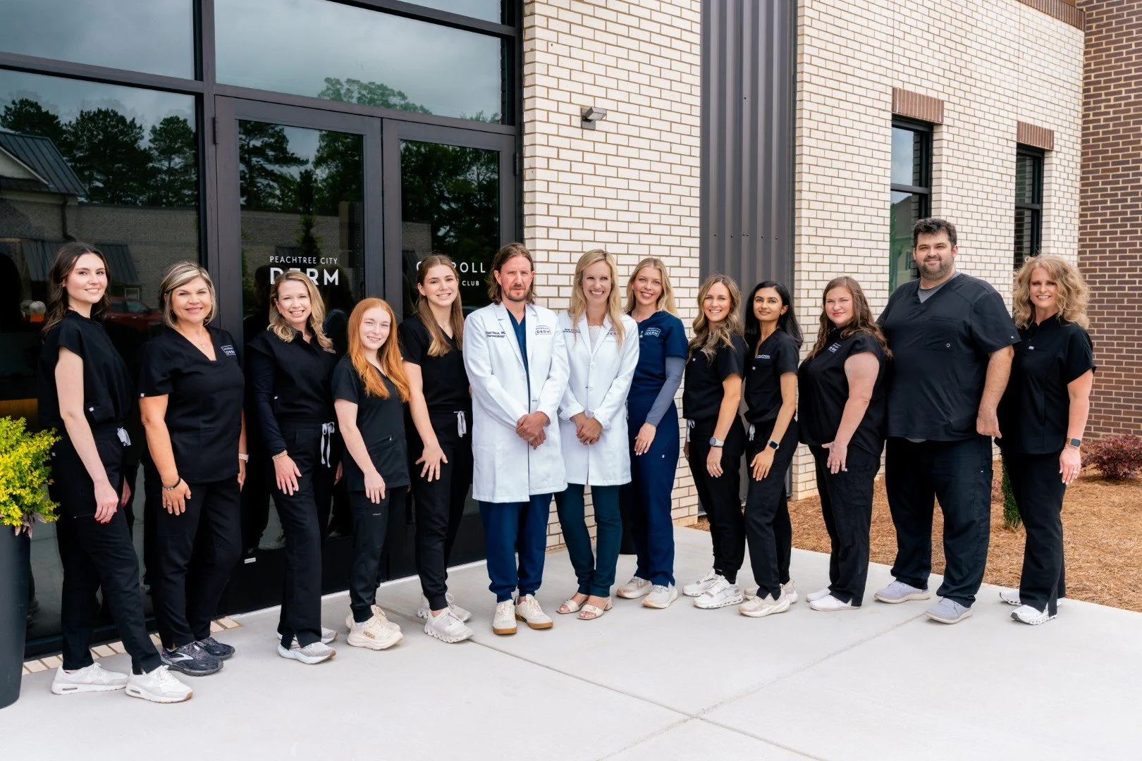 Group of healthcare professionals standing outside the Peachtree City Dream Clinic, dressed in medical scrubs and white coats, smiling for the camera.