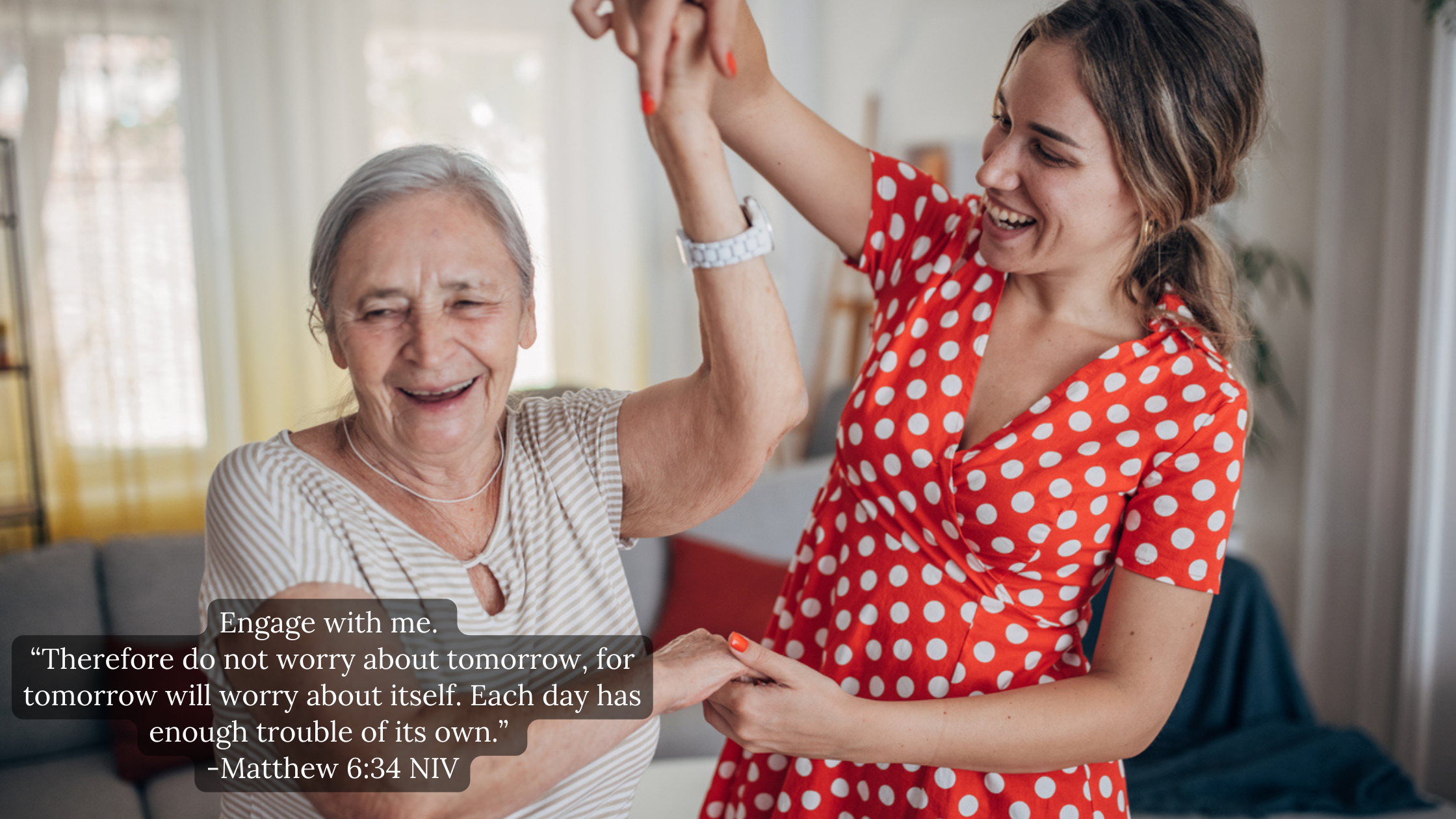 A young woman in a red polka dot dress and an elderly woman in a striped shirt share a joyful moment indoors, holding hands and smiling.