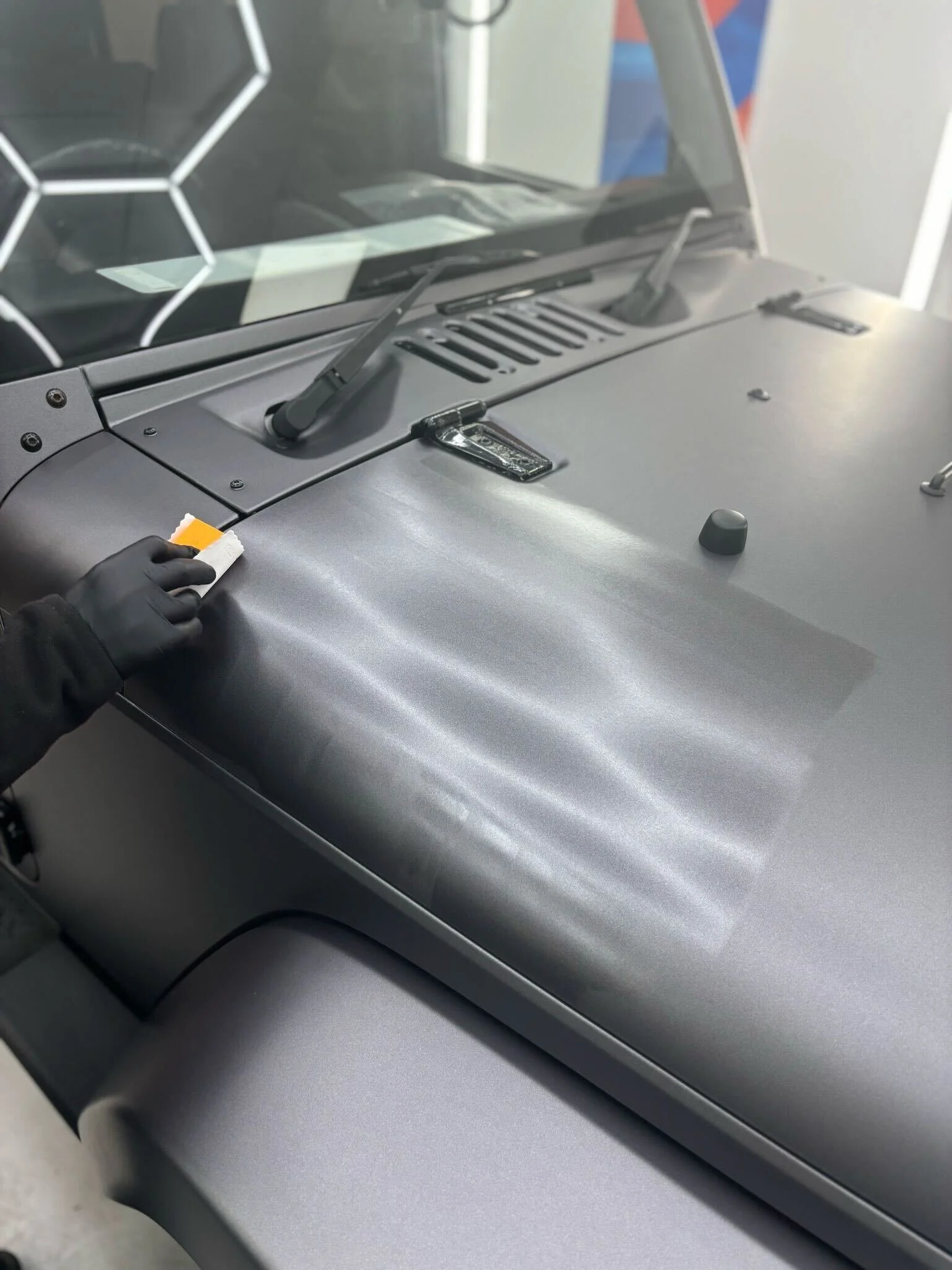 Person cleaning the hood of a vintage silver car with a cloth, wearing black gloves.