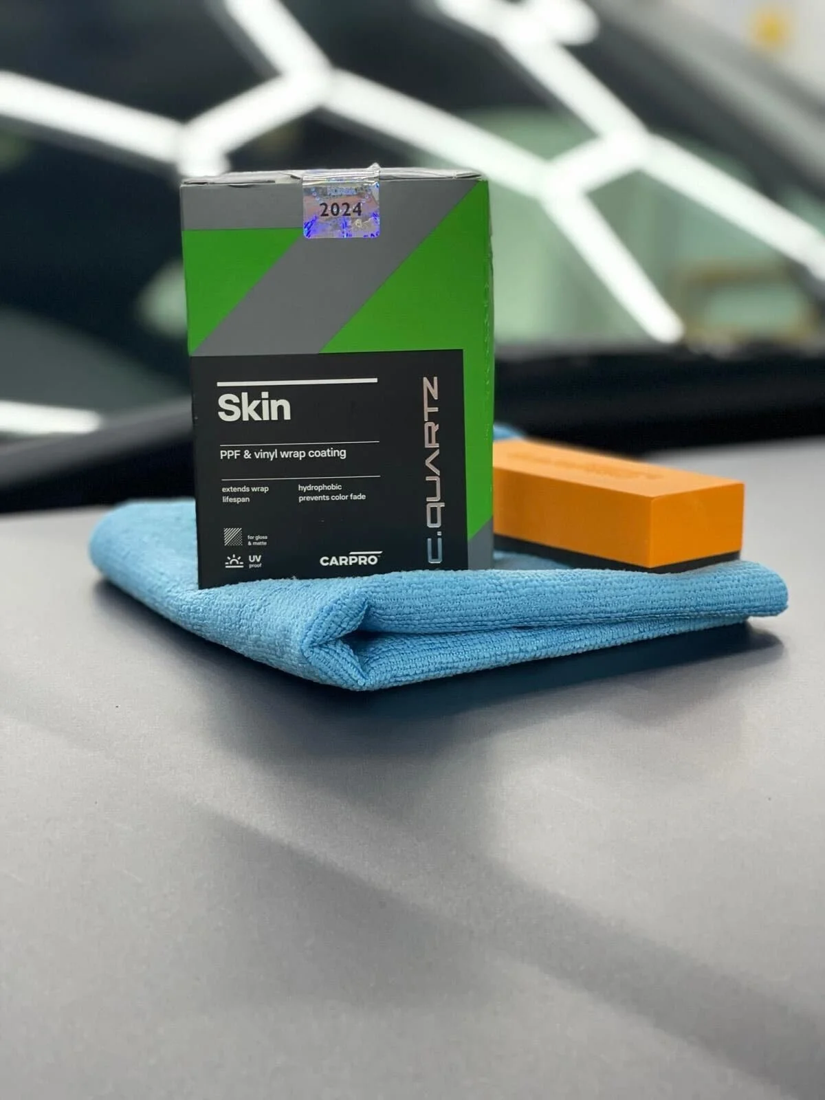 Carpro Skin PPF and vinyl wrap coating box, blue microfiber cloth, and orange sponge on a car dashboard.