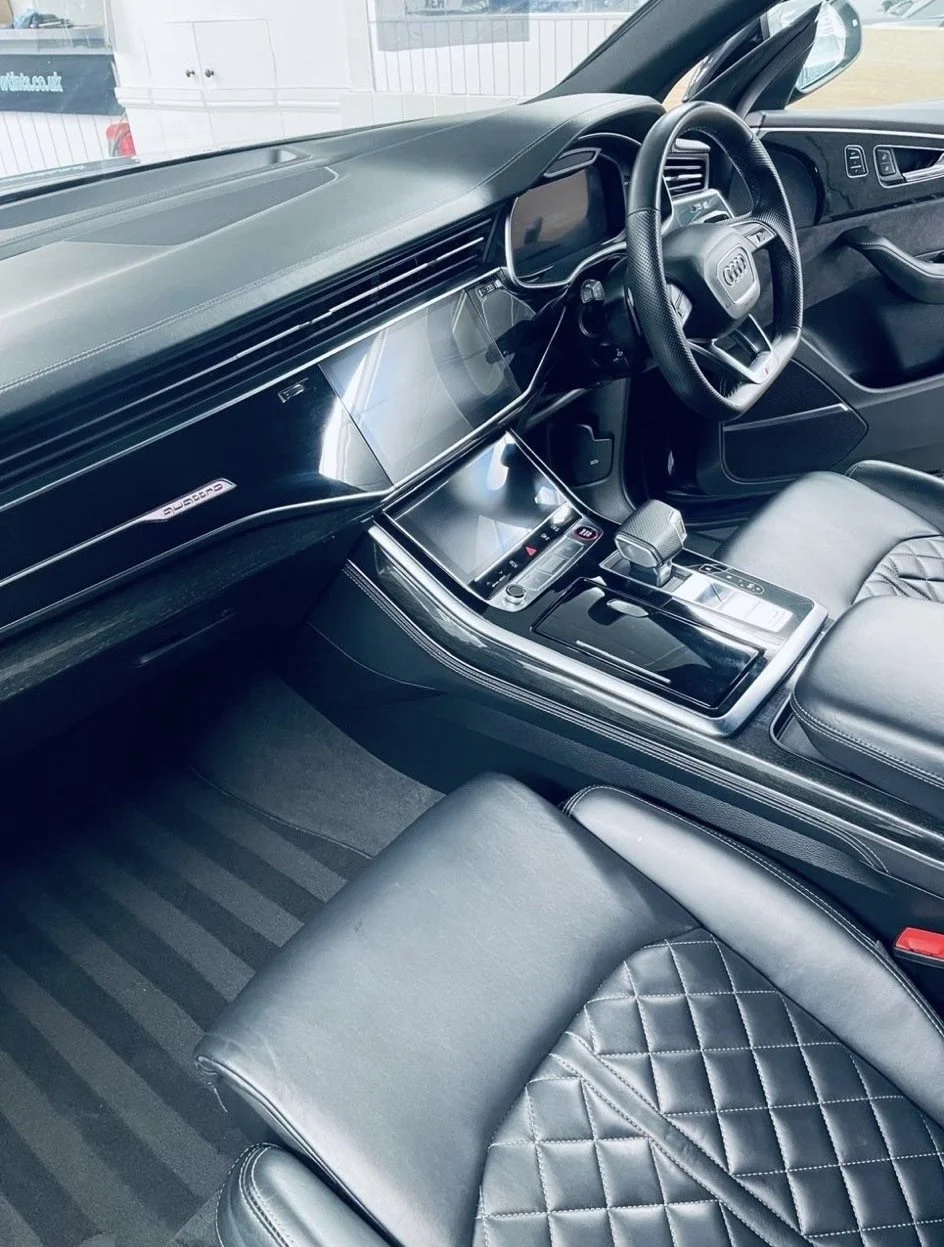 Interior of a modern luxury vehicle featuring a black dashboard, digital displays, quilted leather seats, and a sleek center console with gear shifter.