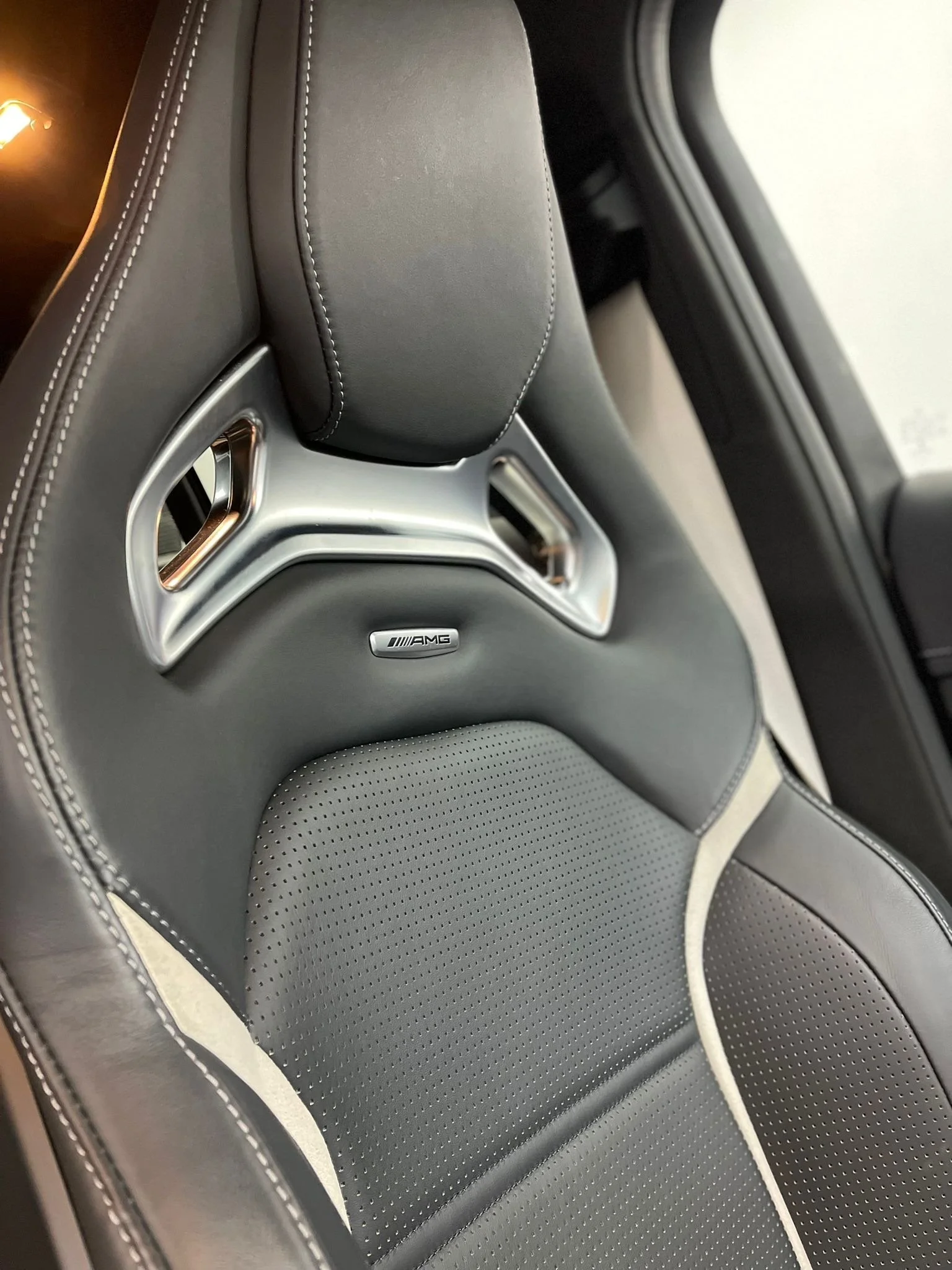 Close-up of a black car seat with AMG branding, perforated leather, and metallic air vent accents.