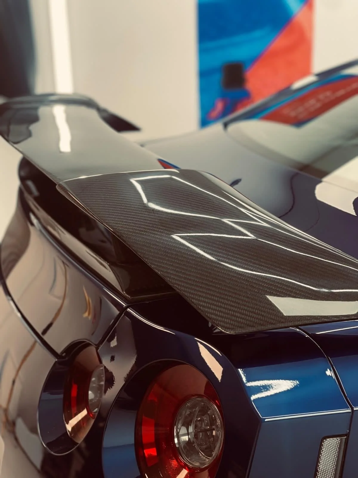 Close-up of a detailed model car showing the rear, with a black body, a carbon fiber spoiler, and red taillights.