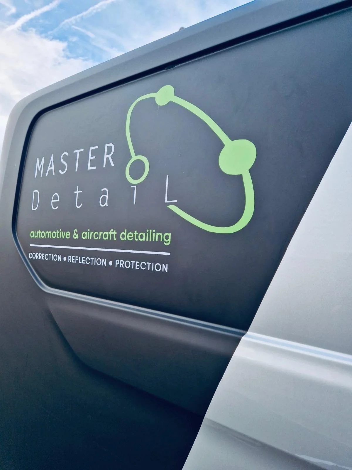 Sign for Master Detail, automotive and aircraft detailing, with a stylized green outline of a car or aircraft part, emphasizing correction, reflection, and protection.