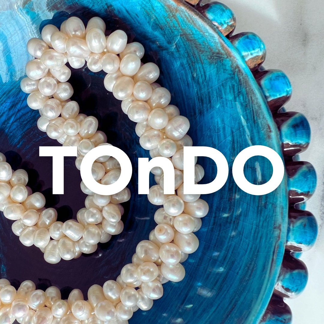 A string of white pearl necklaces resting on a textured blue ceramic plate with scalloped edges.