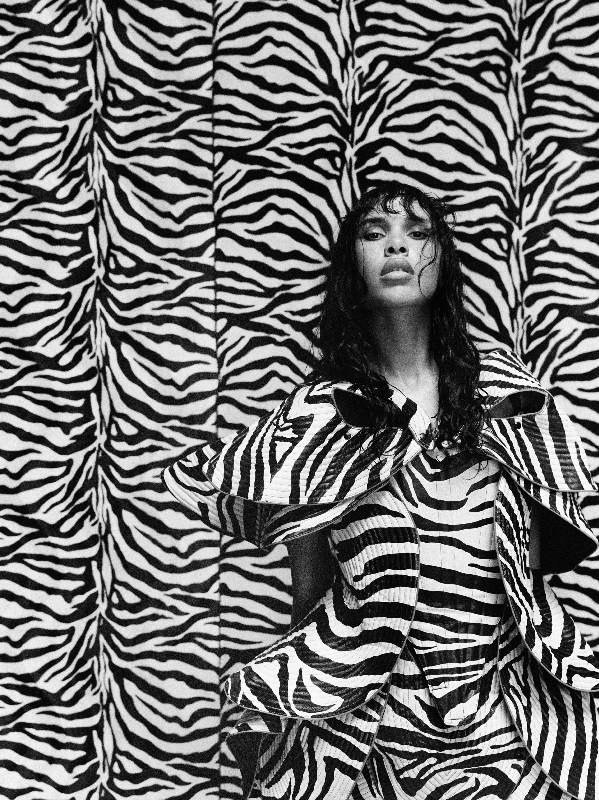 A woman in a zebra print outfit and jacket standing in front of matching zebra print background.