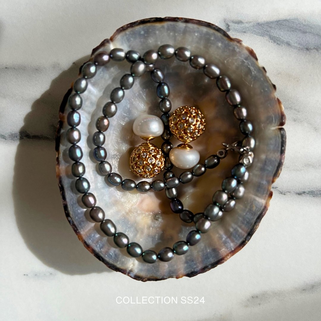 A shell holding a black pearl necklace and gold-and-pearl earrings, with the text 'COLLECTION SS24' at the bottom.