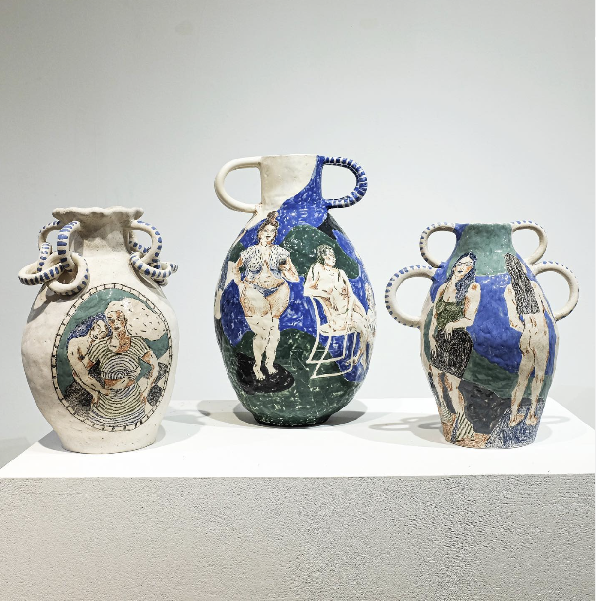 Three decorative ceramic vases with artistic painted scenes of women, displayed on a white pedestal against a plain background.