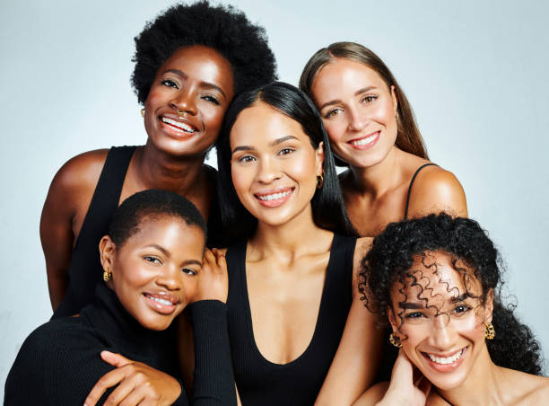Group of five diverse women smiling and posing together against a light background.
