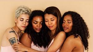 Four women hugging each other in a close group, smiling with their eyes closed.