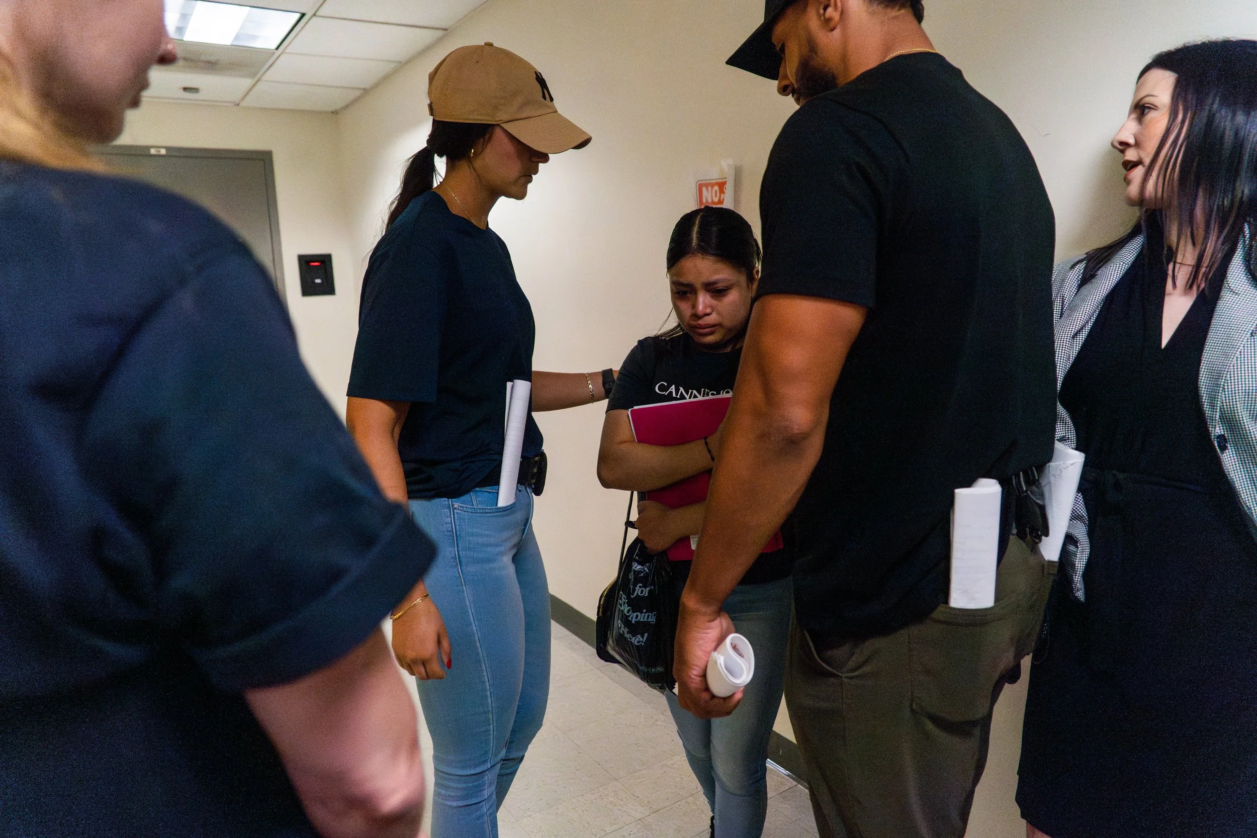 She looked down, crying quietly as officers closed in. The immigration attorney, standing to the right, reminded her she had the right to remain silent—so she said nothing. Moments later, they escorted her away. Her hands gripped her paperwork.