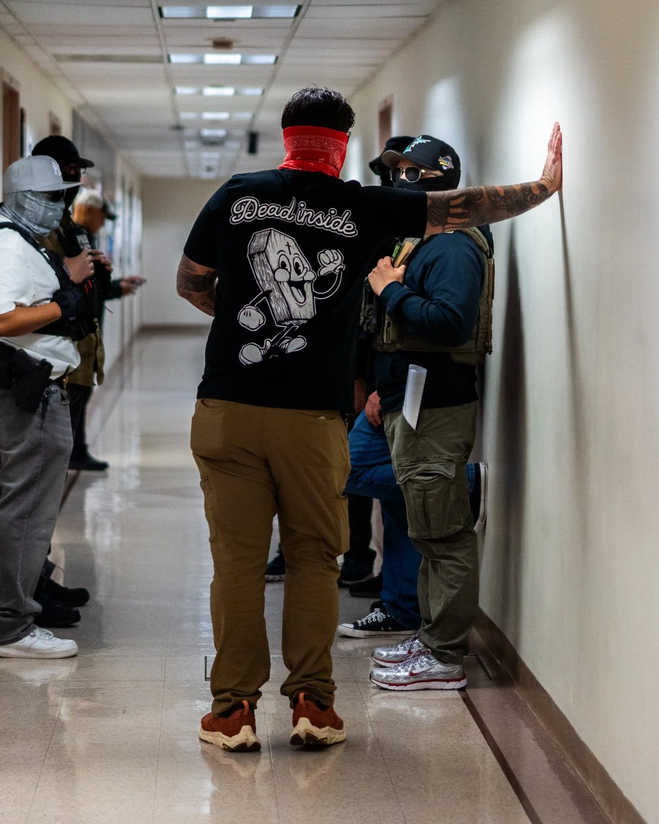 ICE agents line the hallway outside the immigration court, waiting for hearings to end. One leans casually against the wall in a shirt that reads “Dead Inside.” There’s laughter and quiet conversation — a moment of ease before detainments begin again
