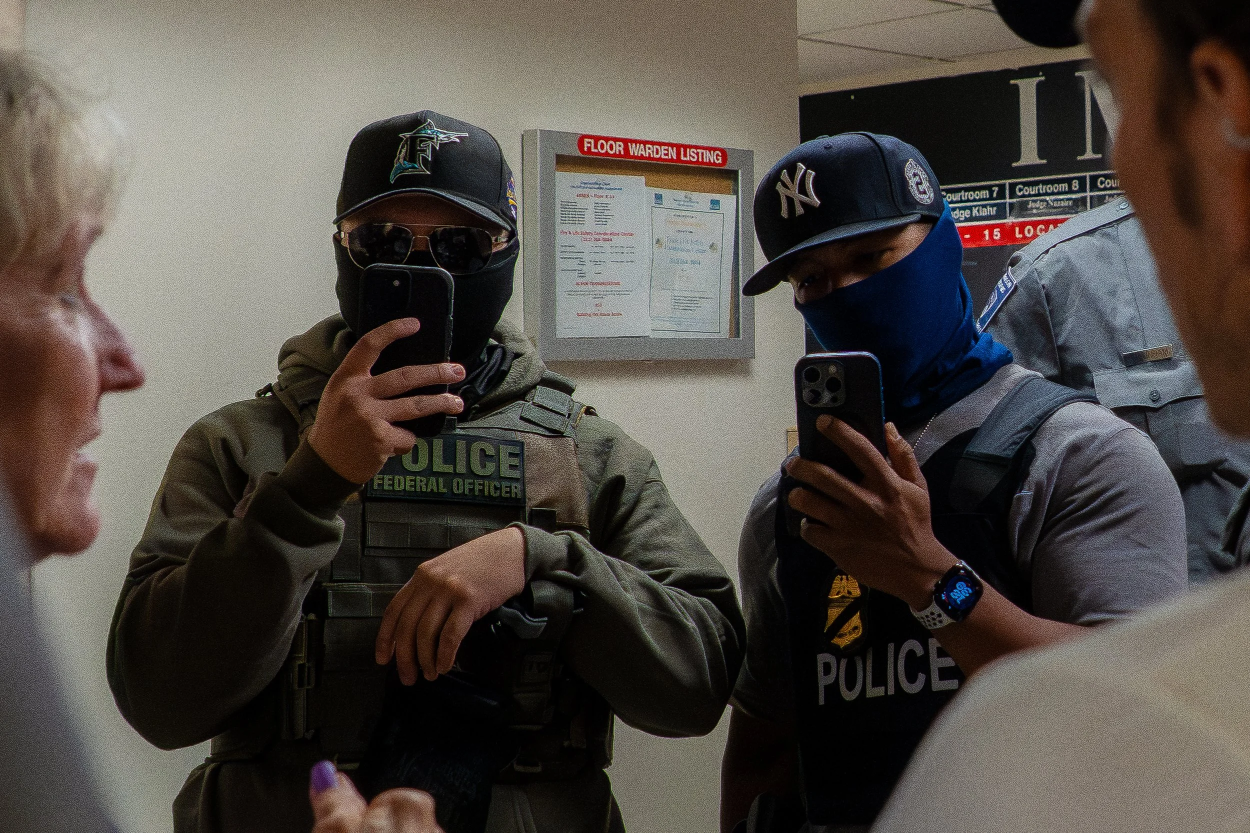 Two ICE agents lift their phones to film the press — capturing journalists as they document arrests.